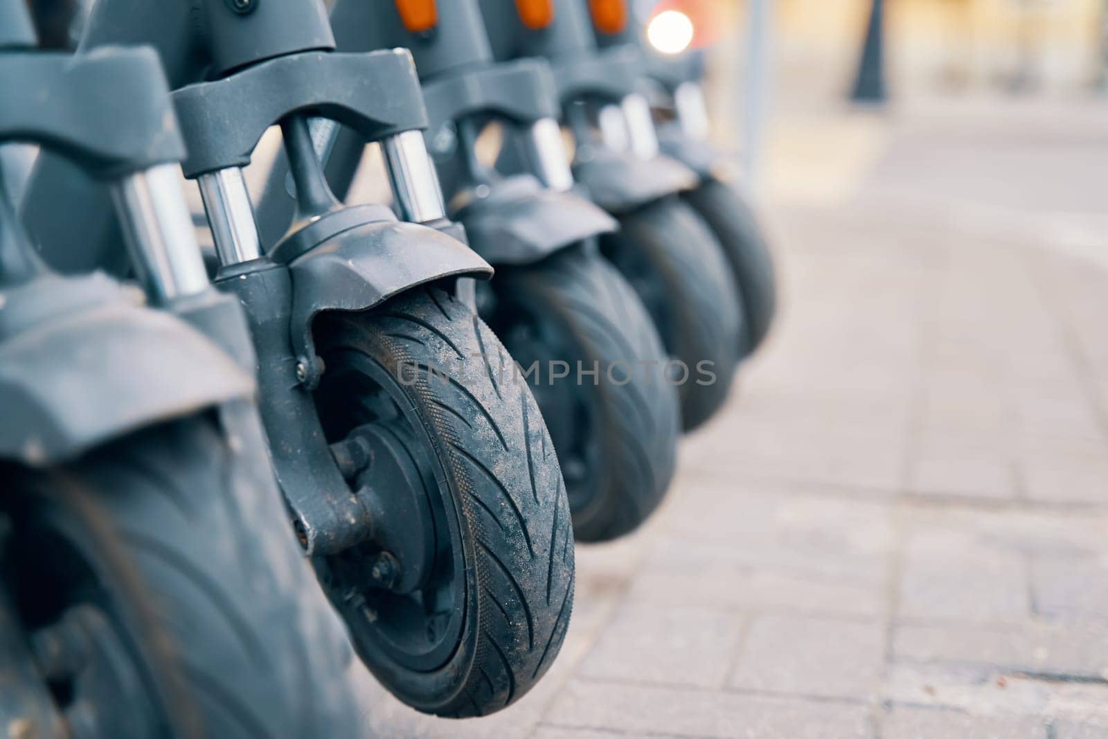 A line of motor vehicles with tires and wheels are parked on the sidewalk, made of synthetic rubber and designed for rolling on asphalt