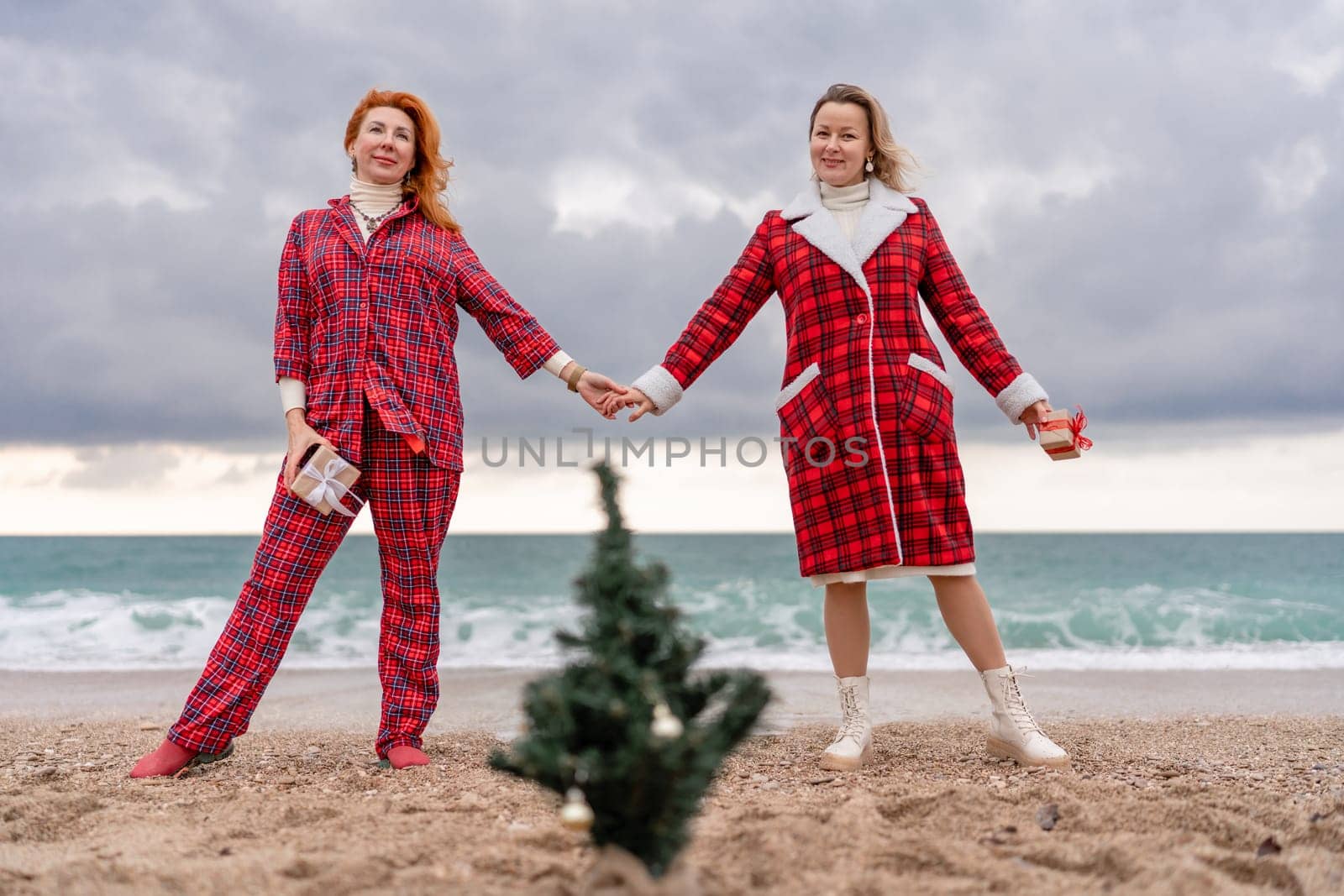 Sea two Lady in plaid shirt with a christmas tree in her hands enjoys beach. Coastal area. Christmas, New Year holidays concep by Matiunina