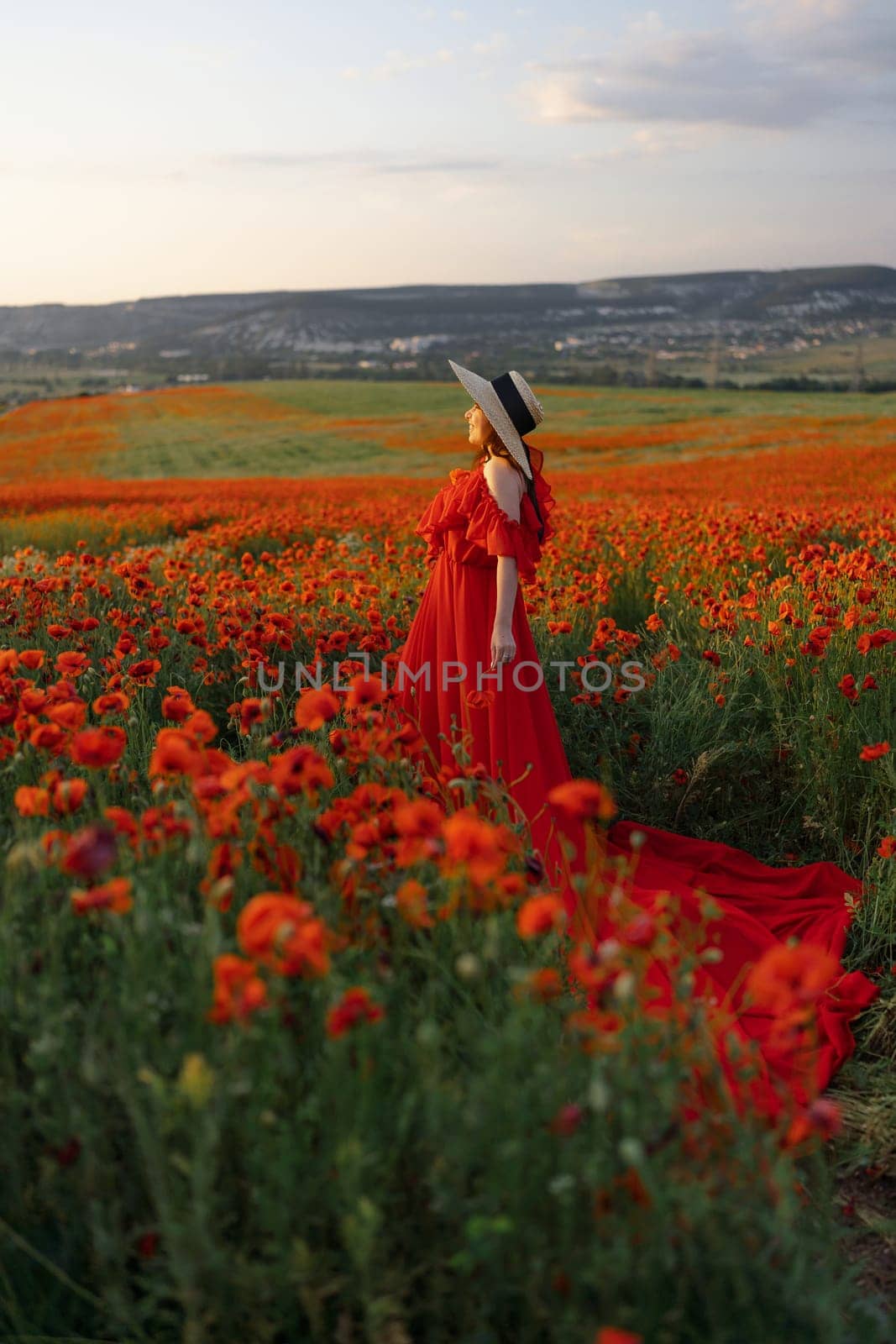 Woman poppy field red dress hat. Happy woman in a long red dress in a beautiful large poppy field. Blond stands with her back posing on a large field of red poppies