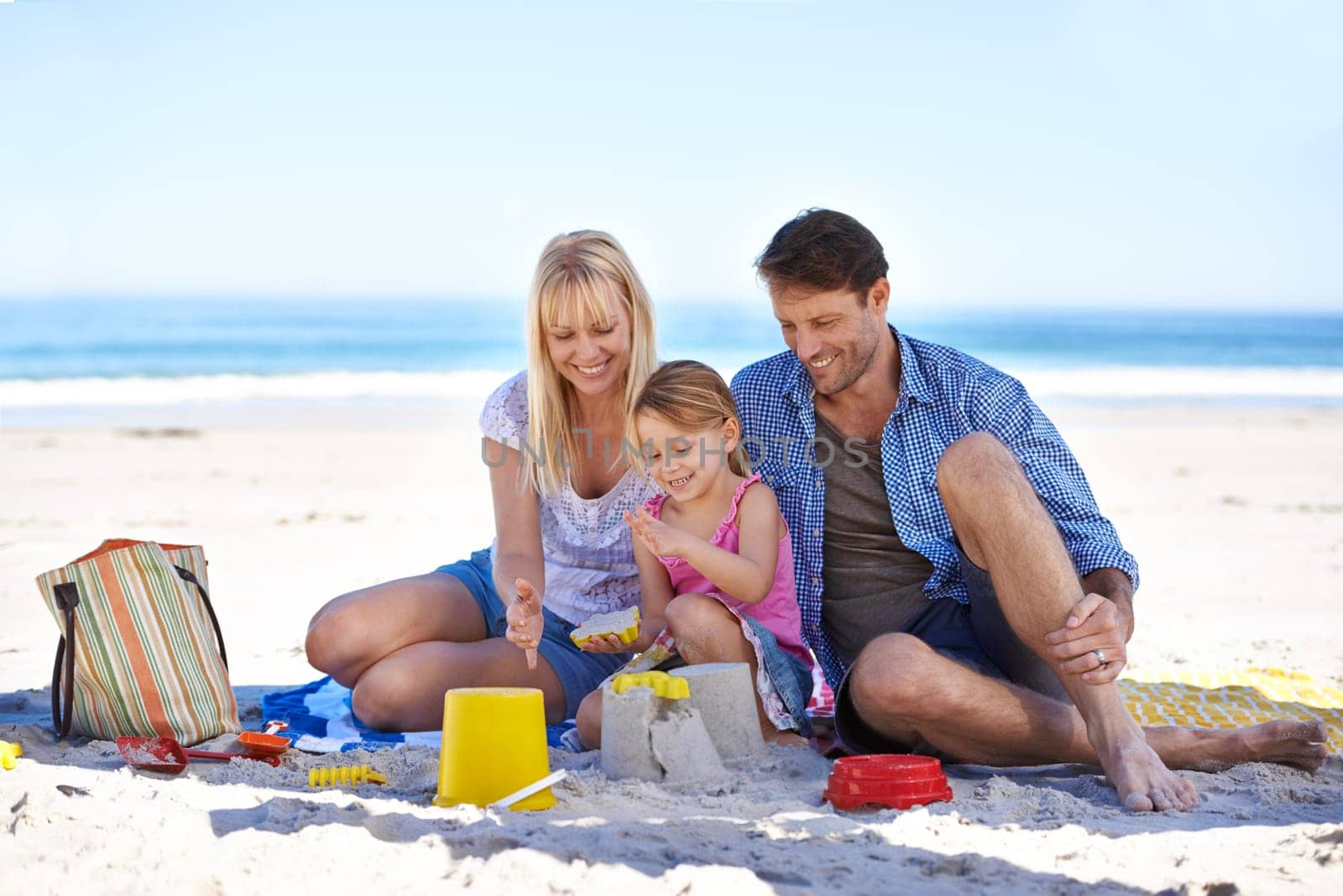 Mom, dad and girl with sandcastle at beach on vacation with care, learning and building on holiday in summer. Father, mother and daughter with plastic bucket with sand for game, play and happy by sea.