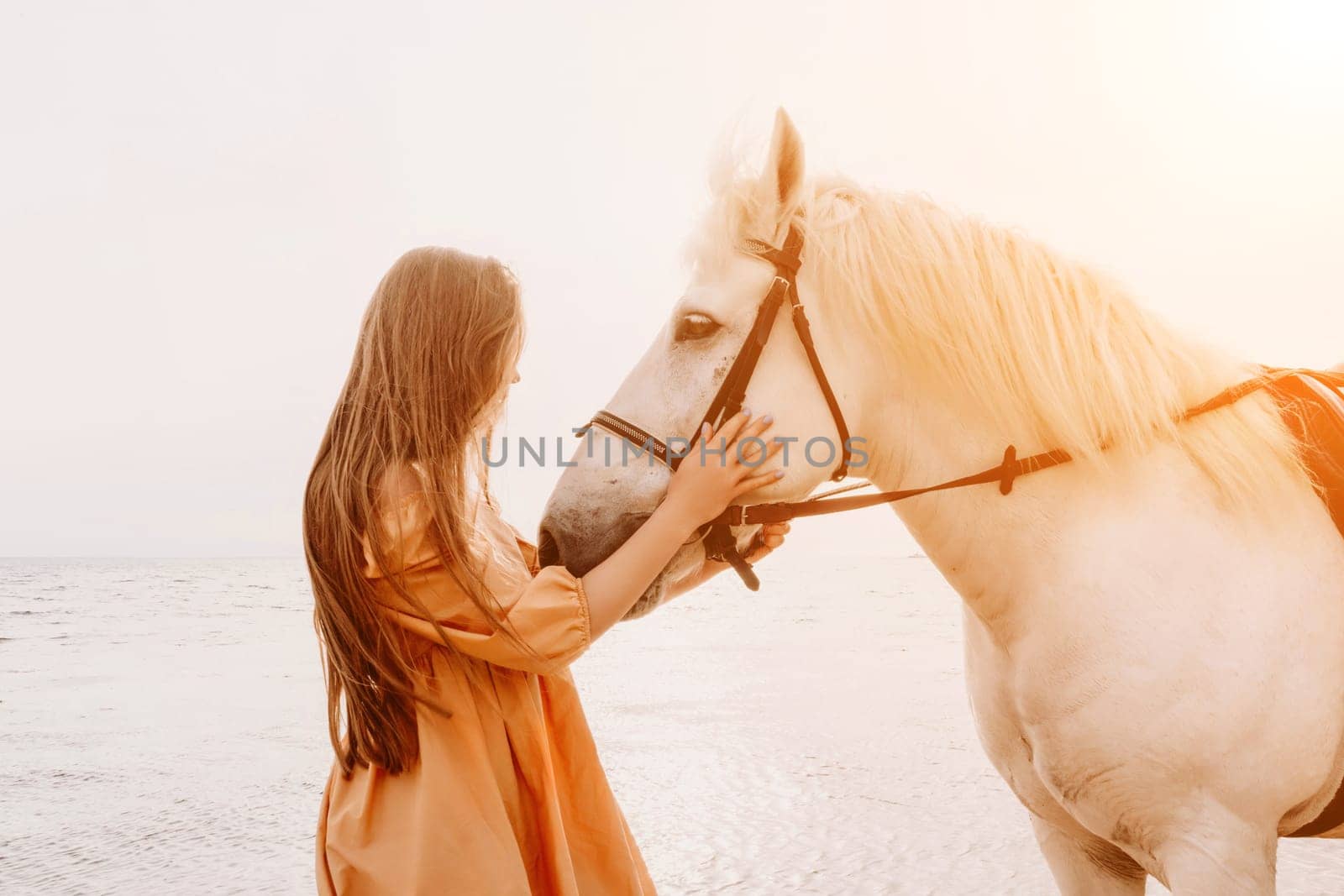 A white horse and a woman in a dress stand on a beach, with the sky and sea creating a picturesque backdrop for the scene