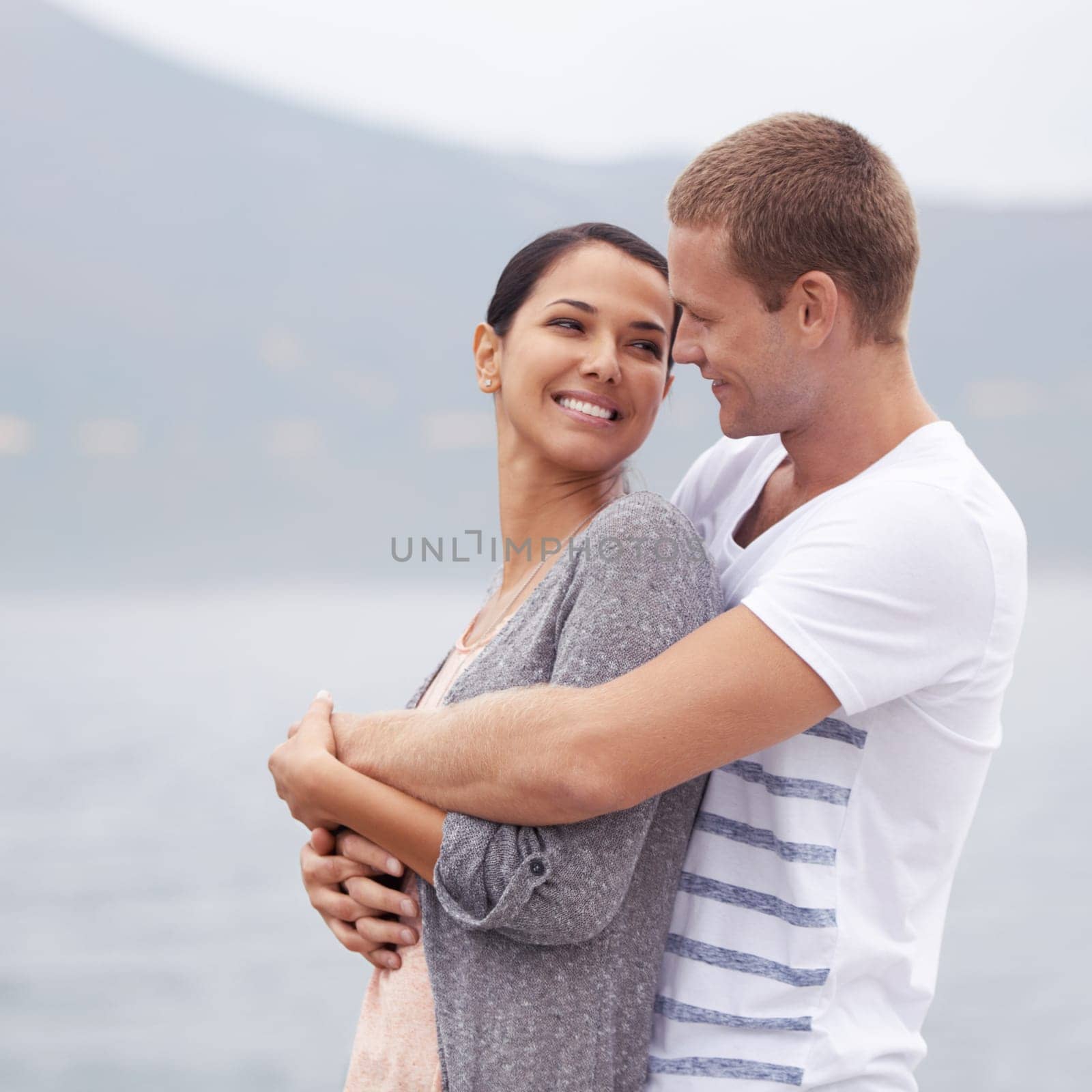 Couple, hug on beach and smile for travel, fresh air with ocean and happiness together outdoor. Romantic adventure, love and affection for bonding, support and trust with commitment on holiday.