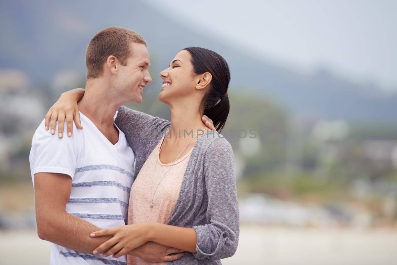 Love, romance and dating for couple at beach for leisure, bonding or vacation. Partners, mates and relationship with smile and hug for kiss and affection against blurred background and mockup.