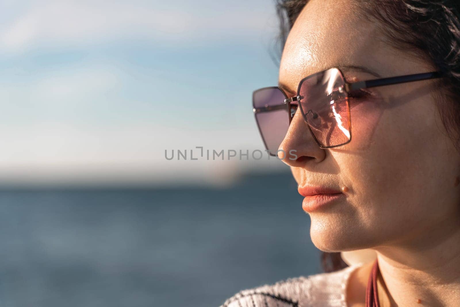 Portrait of a curly woman in glasses on the background of the sea. Vacation on the sea, walk, tourism