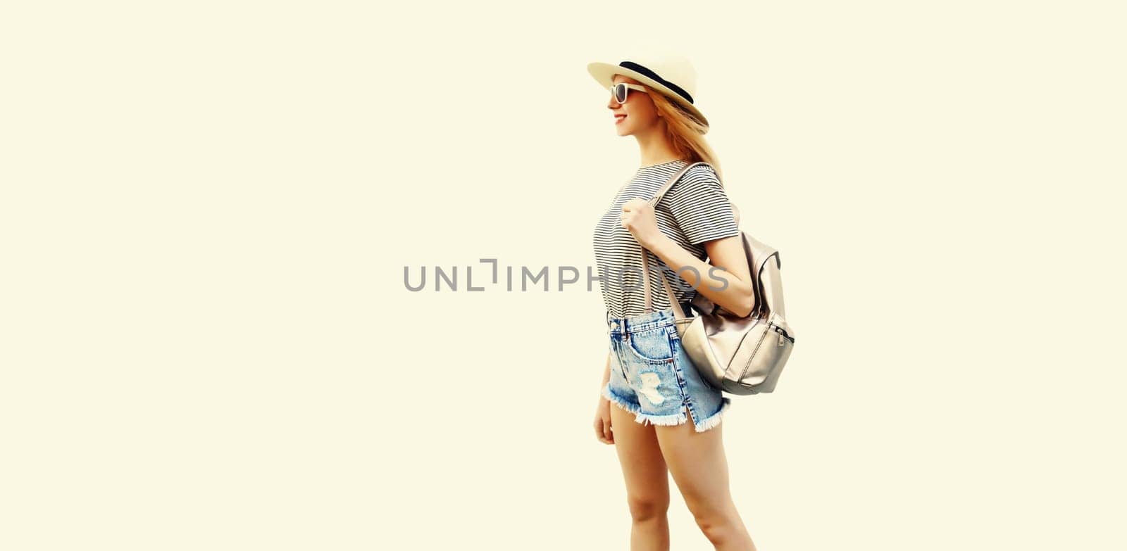 Portrait of smiling young woman wearing summer straw hat, backpack and shorts on white background
