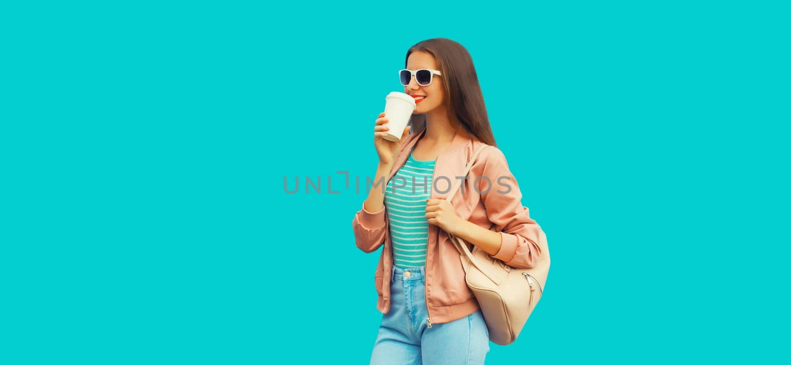 Portrait of smiling young woman drinking coffee wearing backpack on blue background