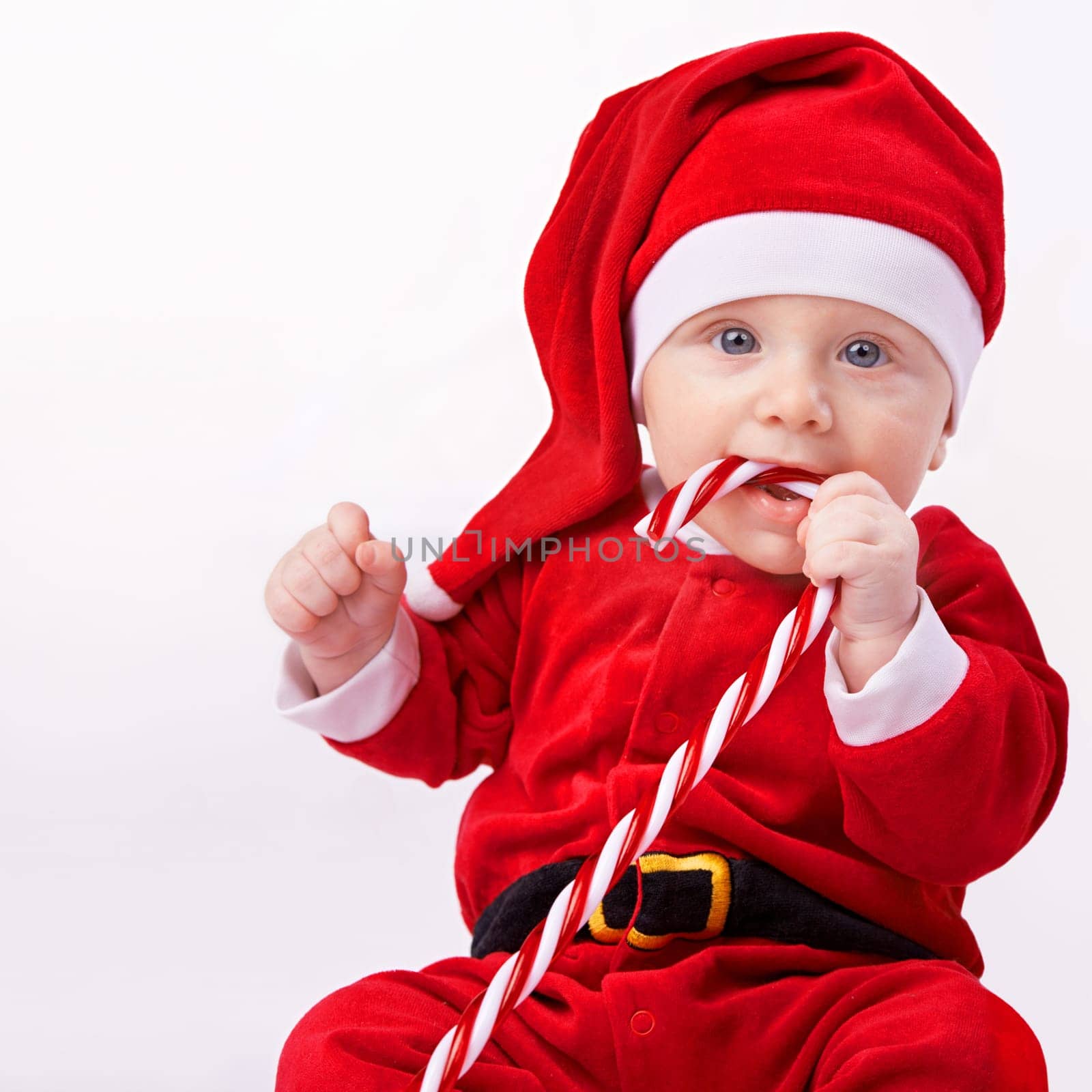 Baby, portrait and studio with santa costume for first Christmas holiday, candy cane and white background. Boy toddler, xmas and outfit for festive season or celebration, innocent and adorable in hat.