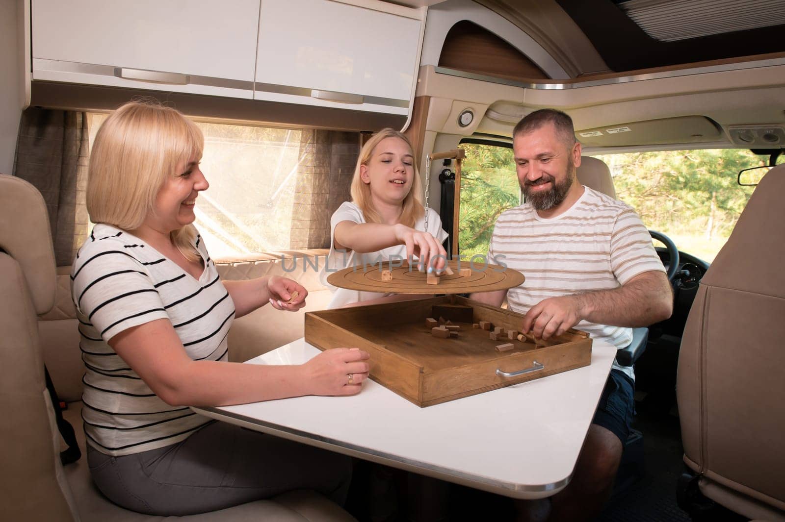 A family of three is playing a board game while sitting in a motorhome by Lobachad