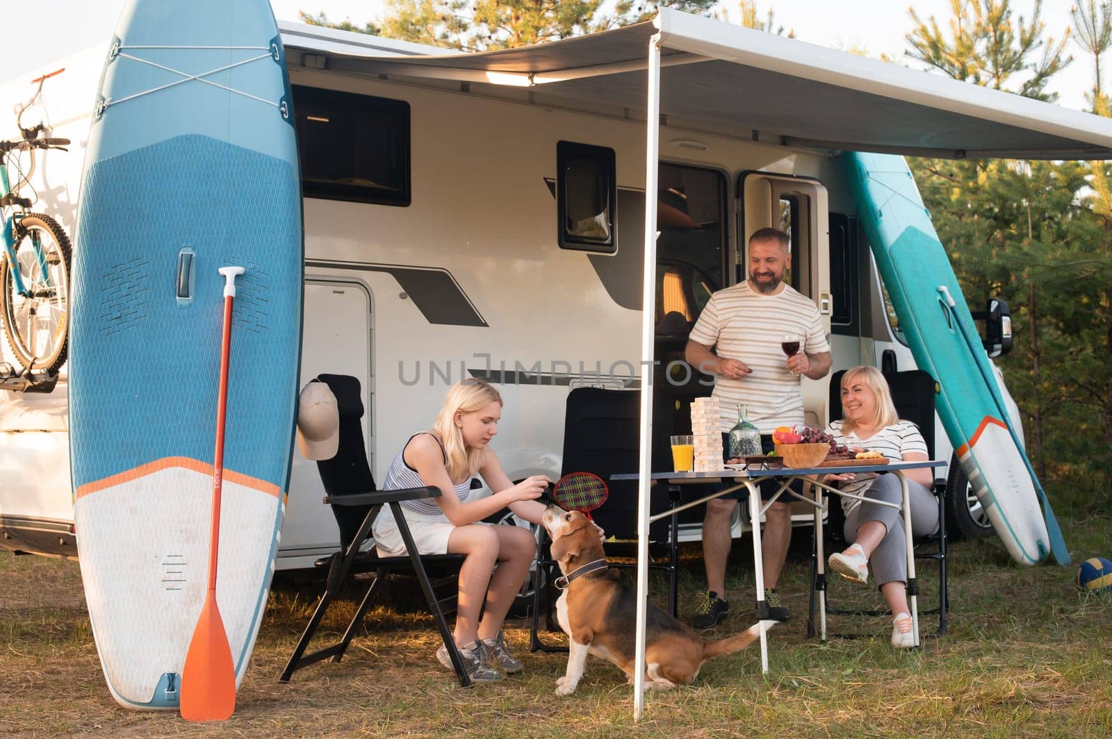 A happy family is resting nearby near their motorhome in the forest.