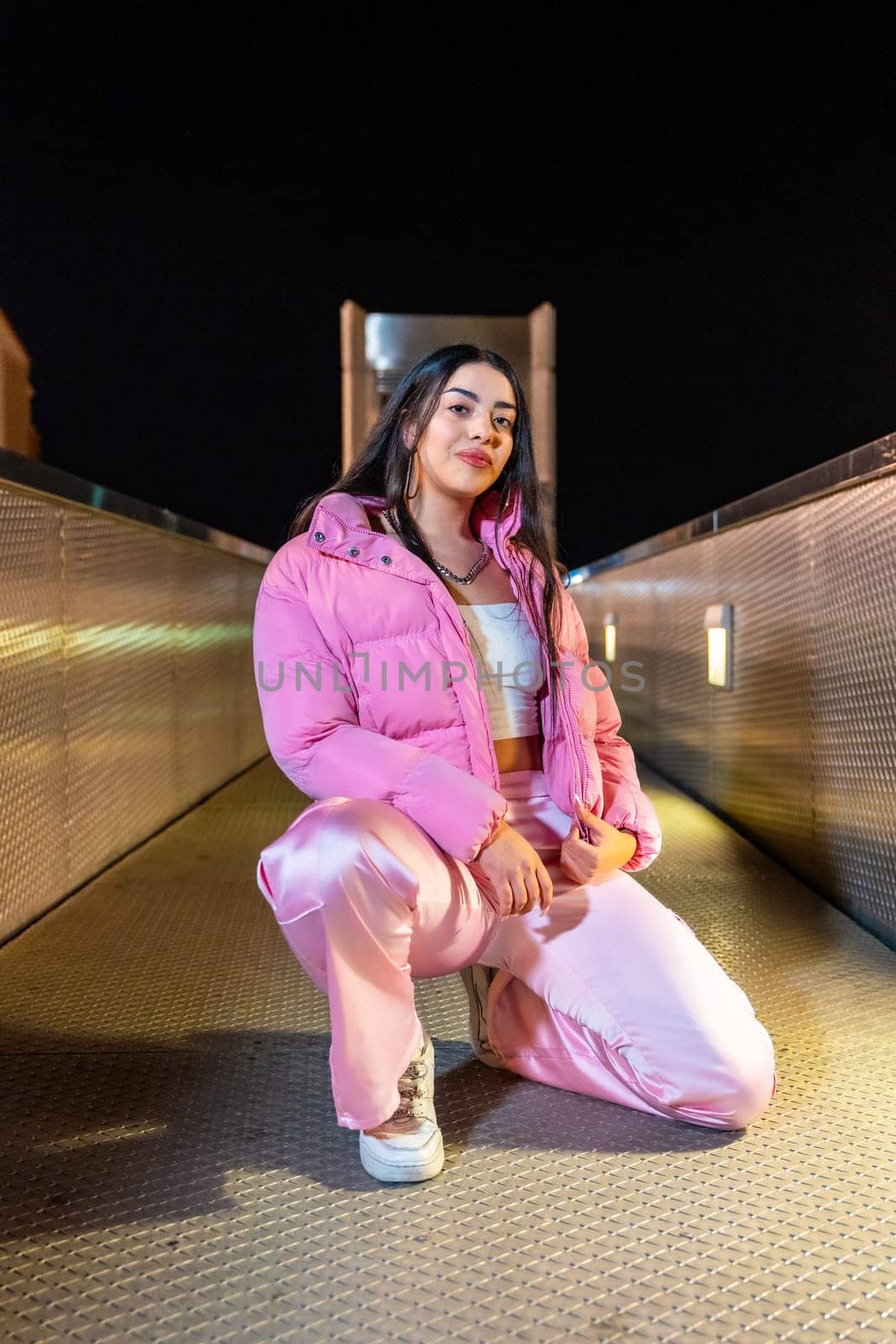 Vertical portrait of a cool breakdancer posing kneeling and looking at camera at night on an urban bridge