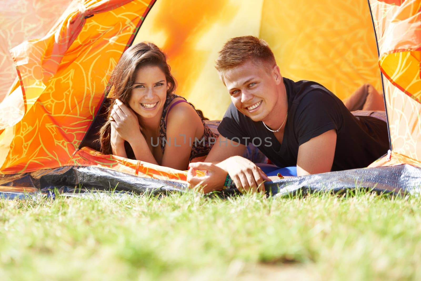 Happy couple, portrait and relax in tent for camping, bonding or outdoor adventure together. Face of young man and woman with smile enjoying fun holiday weekend, vacation or campsite on green grass by YuriArcurs