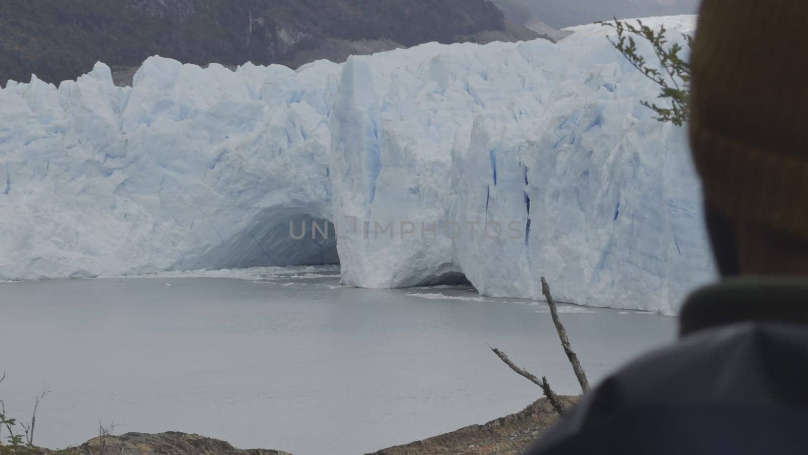Tourist admires Perito Moreno Glacier's immense ice walls from behind, captured in a photo.