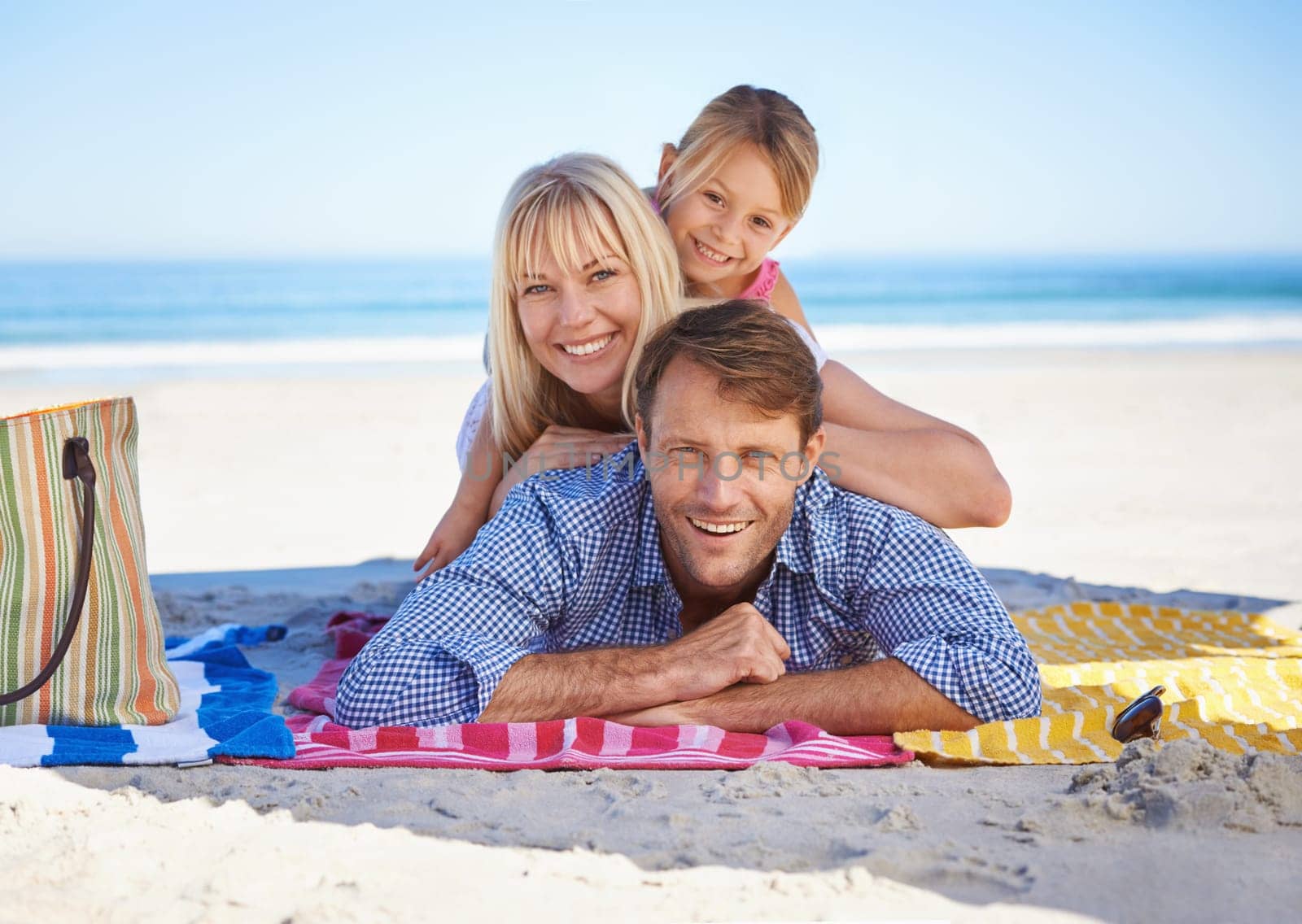 Parents, girl and portrait on blanket at beach with care, love and bonding in summer to relax on holiday. Father, mother and daughter with picnic, connection and happy by sea in sunshine on vacation by YuriArcurs