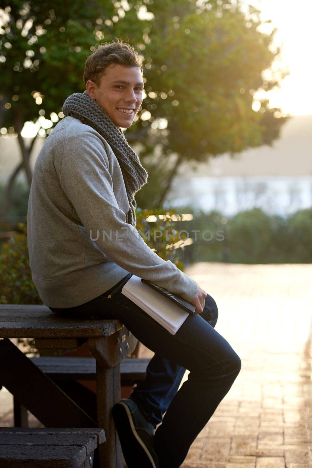 Student, man and outdoor on campus with book in smile, study and prepare for exam with revision notes. Portrait, college and academic for assignment with textbook for education and learning