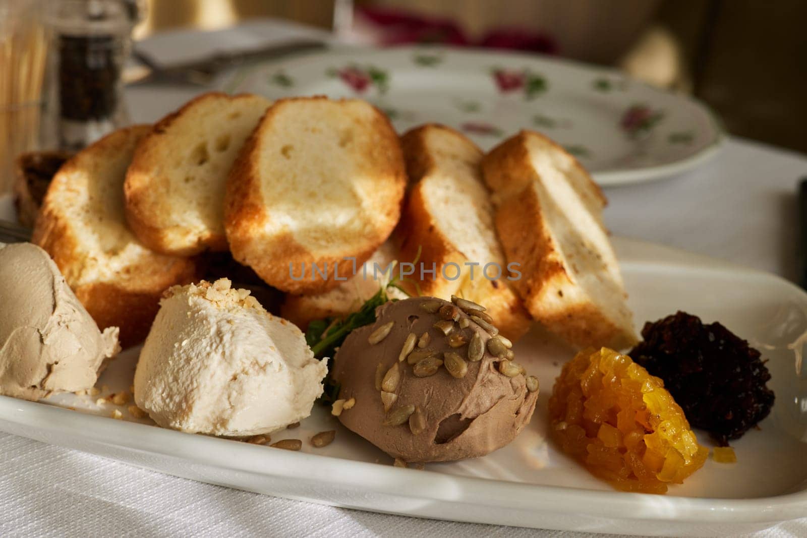 Fresh homemade chicken liver pate on bread over rustic background. Fried toast bread on plates with assorted pates on the kitchen table in the sun