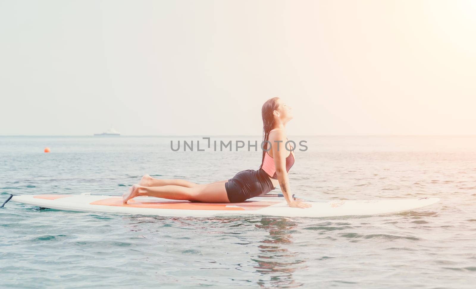 Woman sup yoga. Happy young sporty woman practising yoga pilates on paddle sup surfboard. Female stretching doing workout on sea water. Modern individual female outdoor summer sport activity