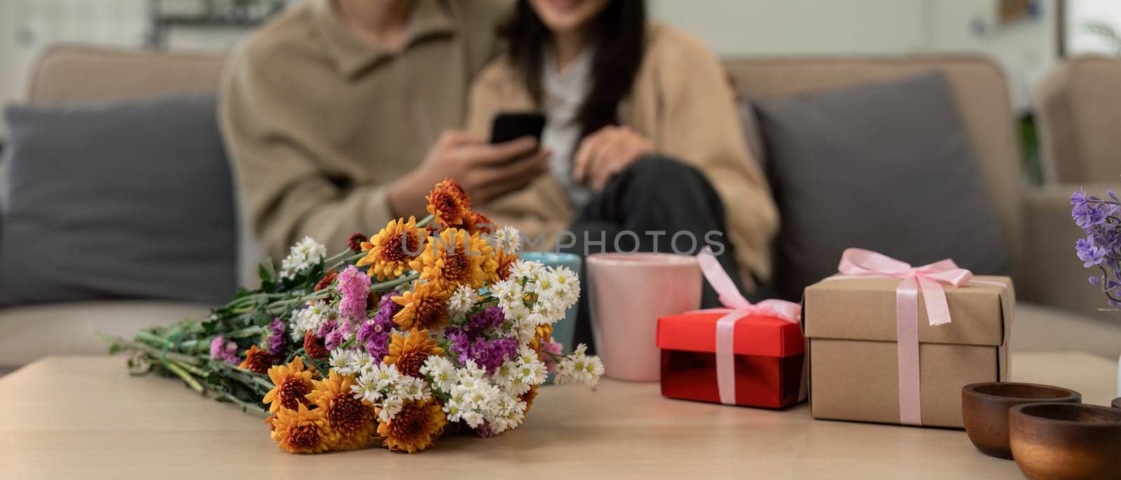Romantic young asian couple embracing with holding flowers and smiling in living room at home. fall in love. Valentine concept.