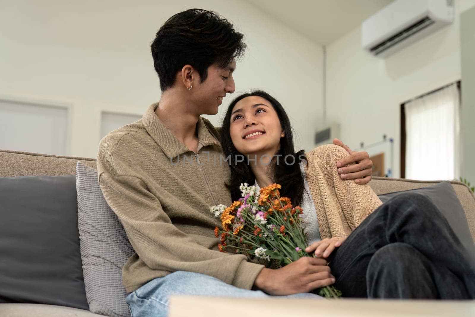 Romantic young asian couple embracing with holding flowers and smiling in living room at home. fall in love. Valentine concept by nateemee