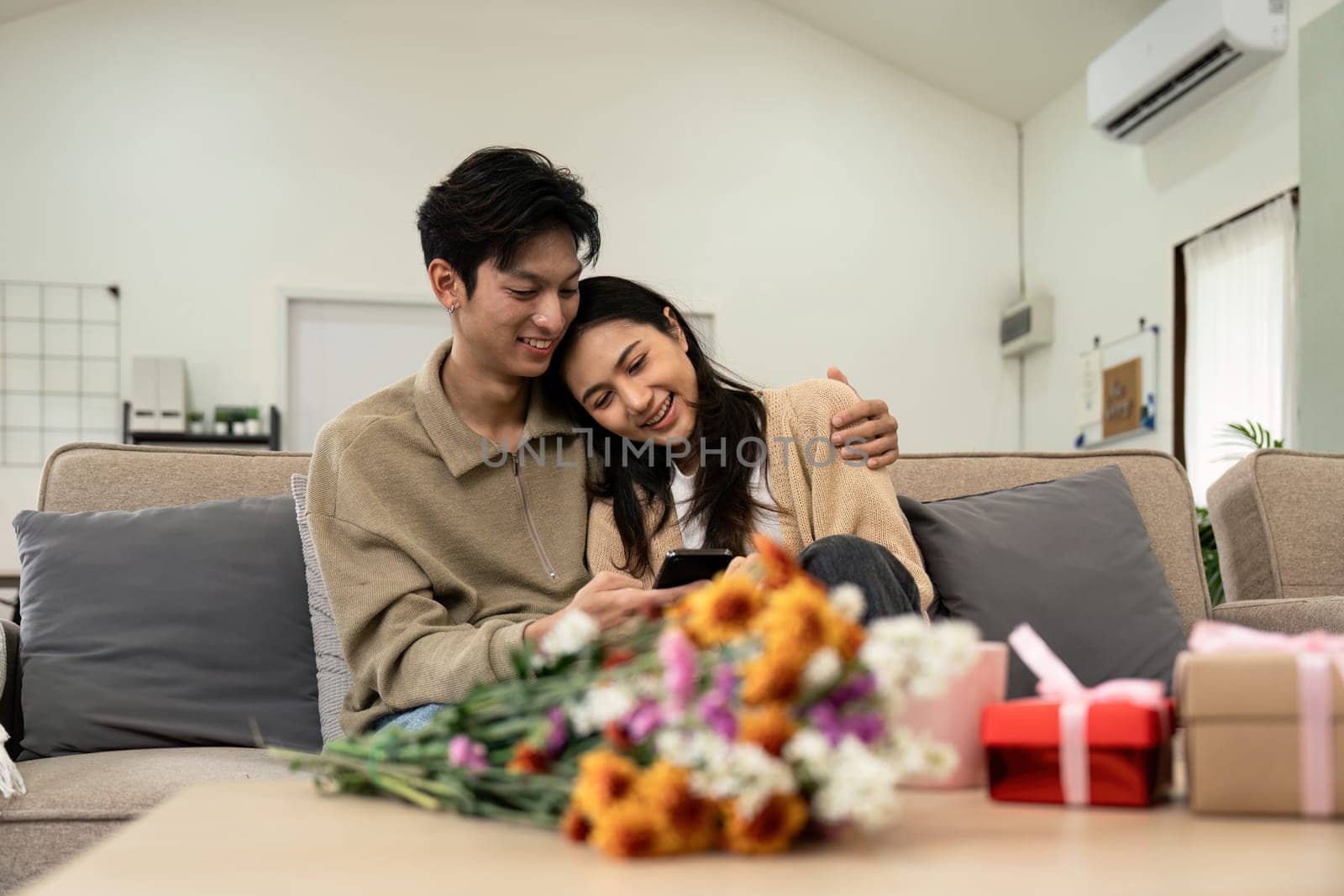 Asian couple lifestyle using phones, shopping or chatting online, sitting on couch at home, holding smartphones, enjoy leisure time. fall in love. Valentine concept.