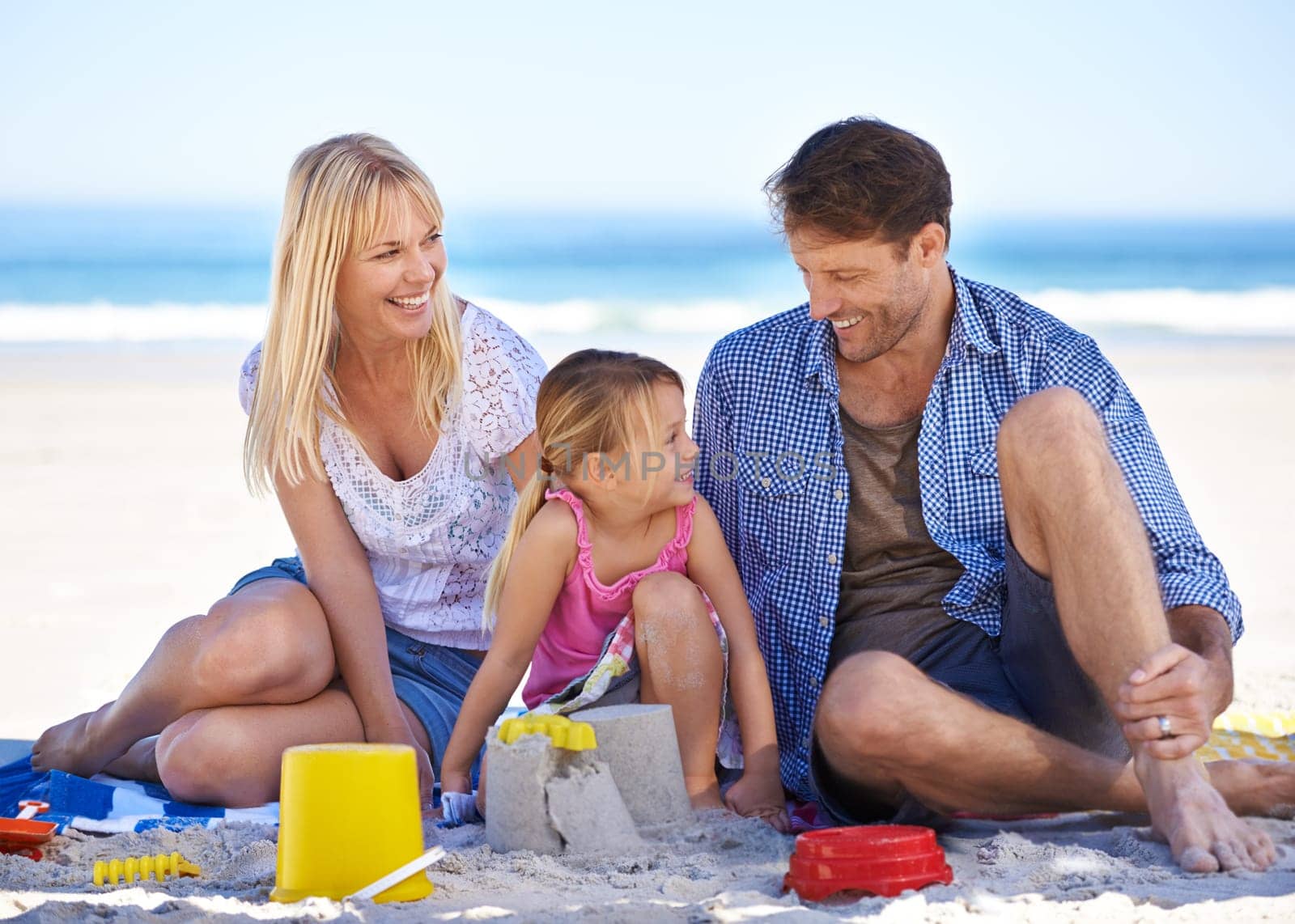 Mom, dad and girl with sandcastle by ocean on vacation with care, learning or building on holiday in summer. Father, mother and daughter with plastic bucket at beach for game, blanket or happy by sea.