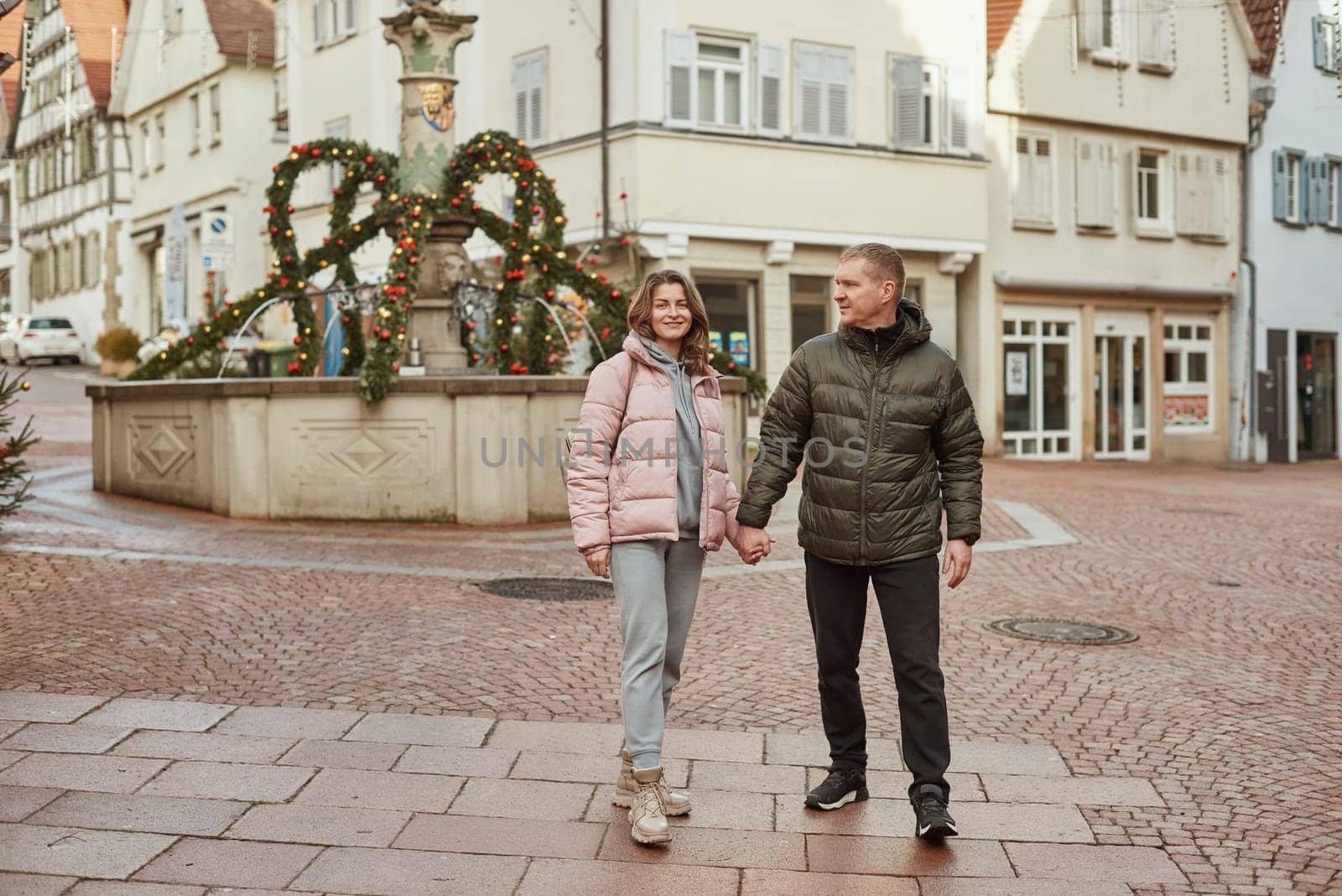 Loving couple of tourists walking around old town. Couple of lovers leisurely stroll in the cool autumn morning on the streets of a BIETIGHEIM-BISSINGEN (Germany). The guy holds his wife. Vacation, Winter, holiday. Romantic Stroll through Historic German Charm. Couple Walking in Europe's Old Town by Andrii_Ko