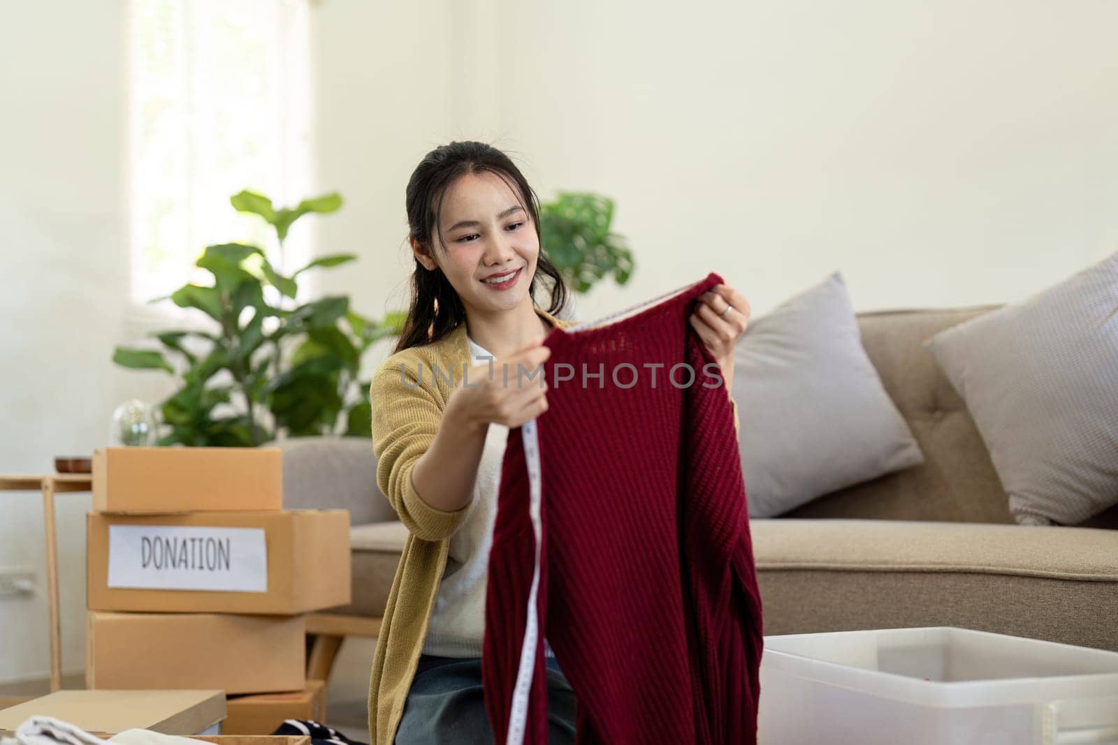 Woman asian holding donation box full with clothes and select clothes. Concept of donation and clothes recycling. Helping poor people.