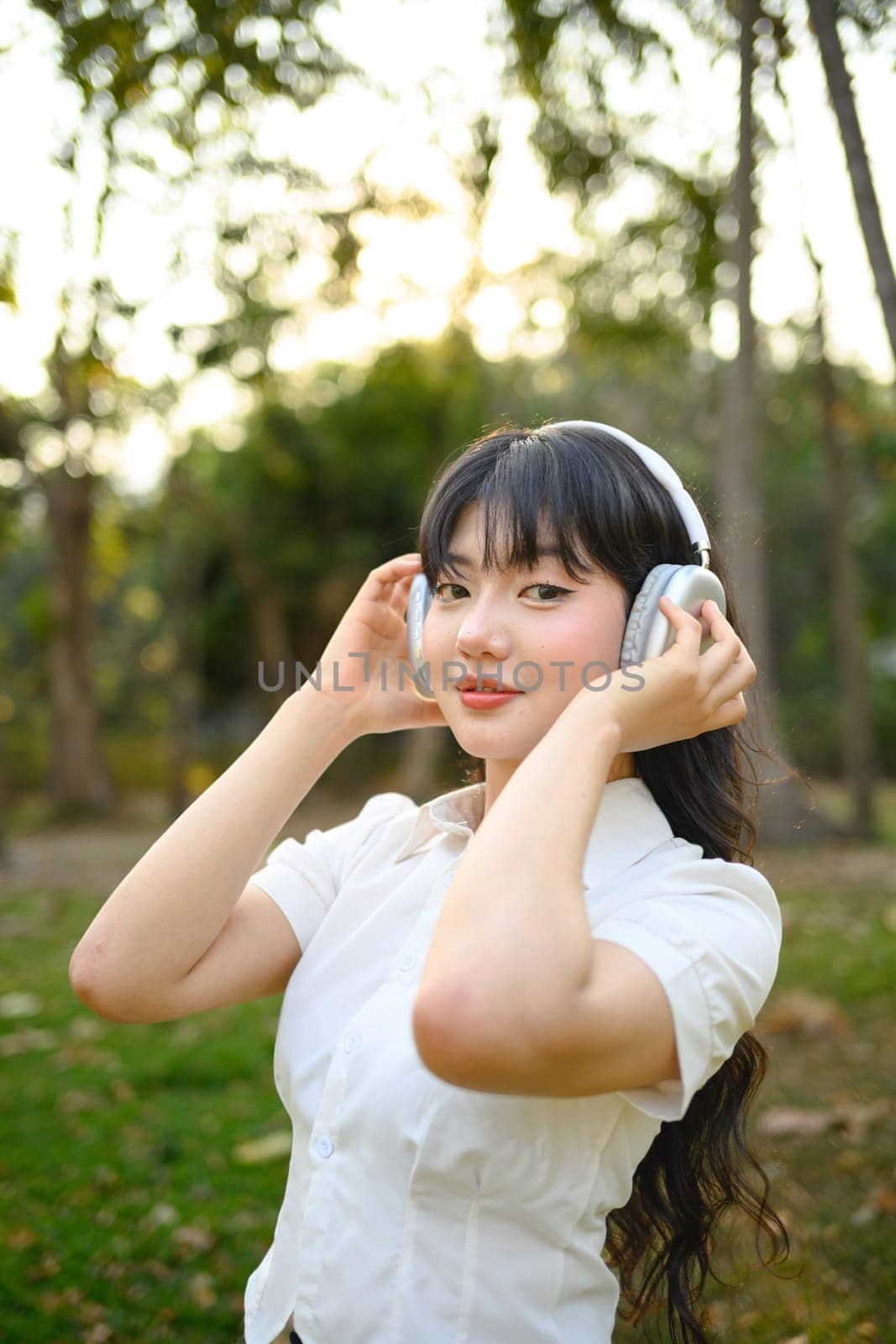 Attractive young woman listening music with headphones, relaxing in the park.