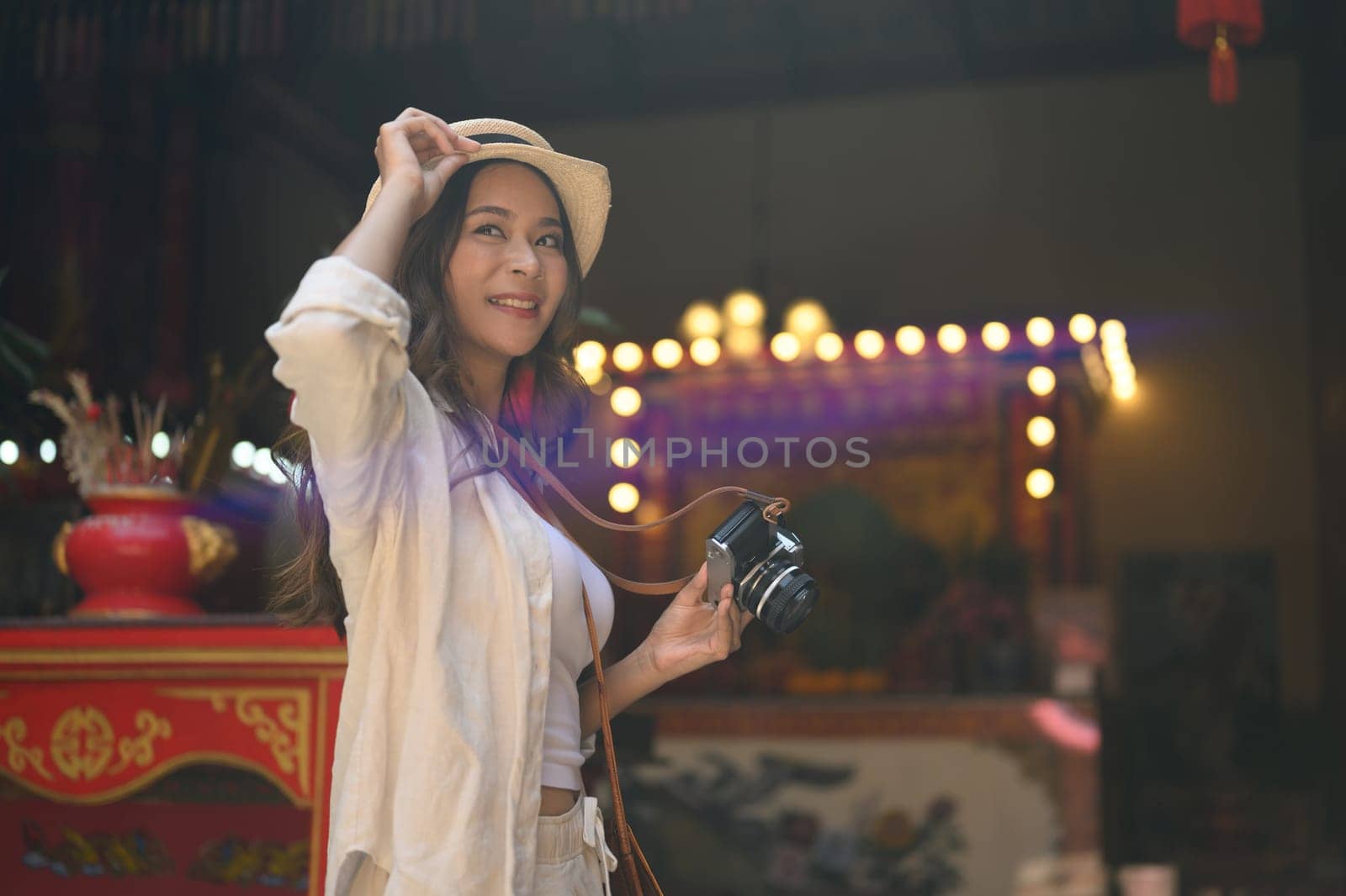 Happy young woman tourist holding camera standing against a Chinese Temple.