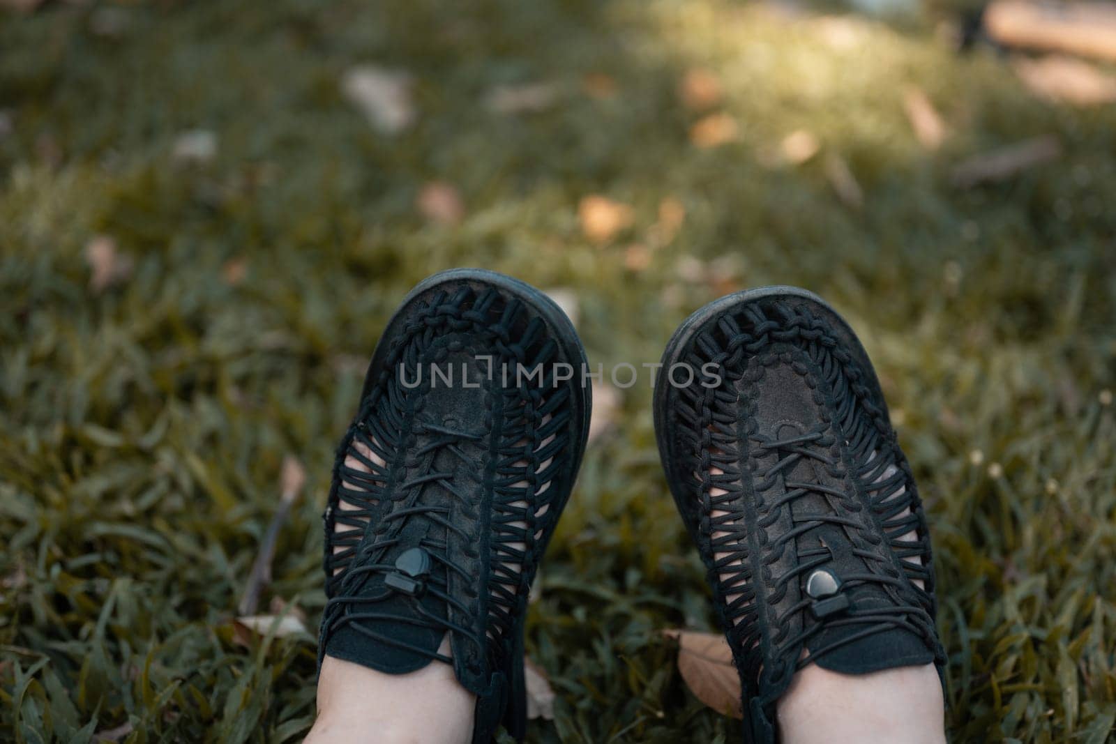 Close up male feet in sneakers on green lawn dappled with sunlight.