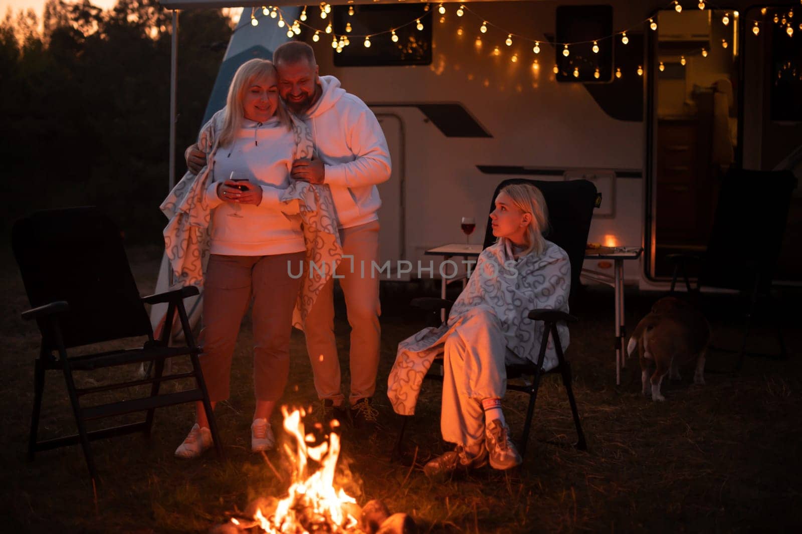 The family is relaxing together by the campfire near their mobile home. Evening family vacation.