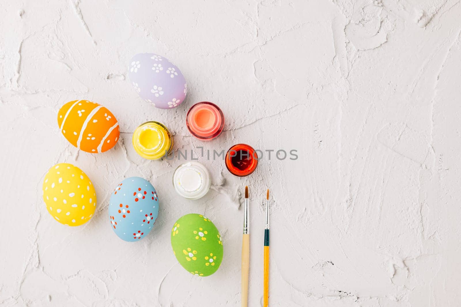 Easter Day Concept. colored multi-colored and paints brush painting easter eggs, colorful paints and paint brushes isolated on white cement background with copy space for text