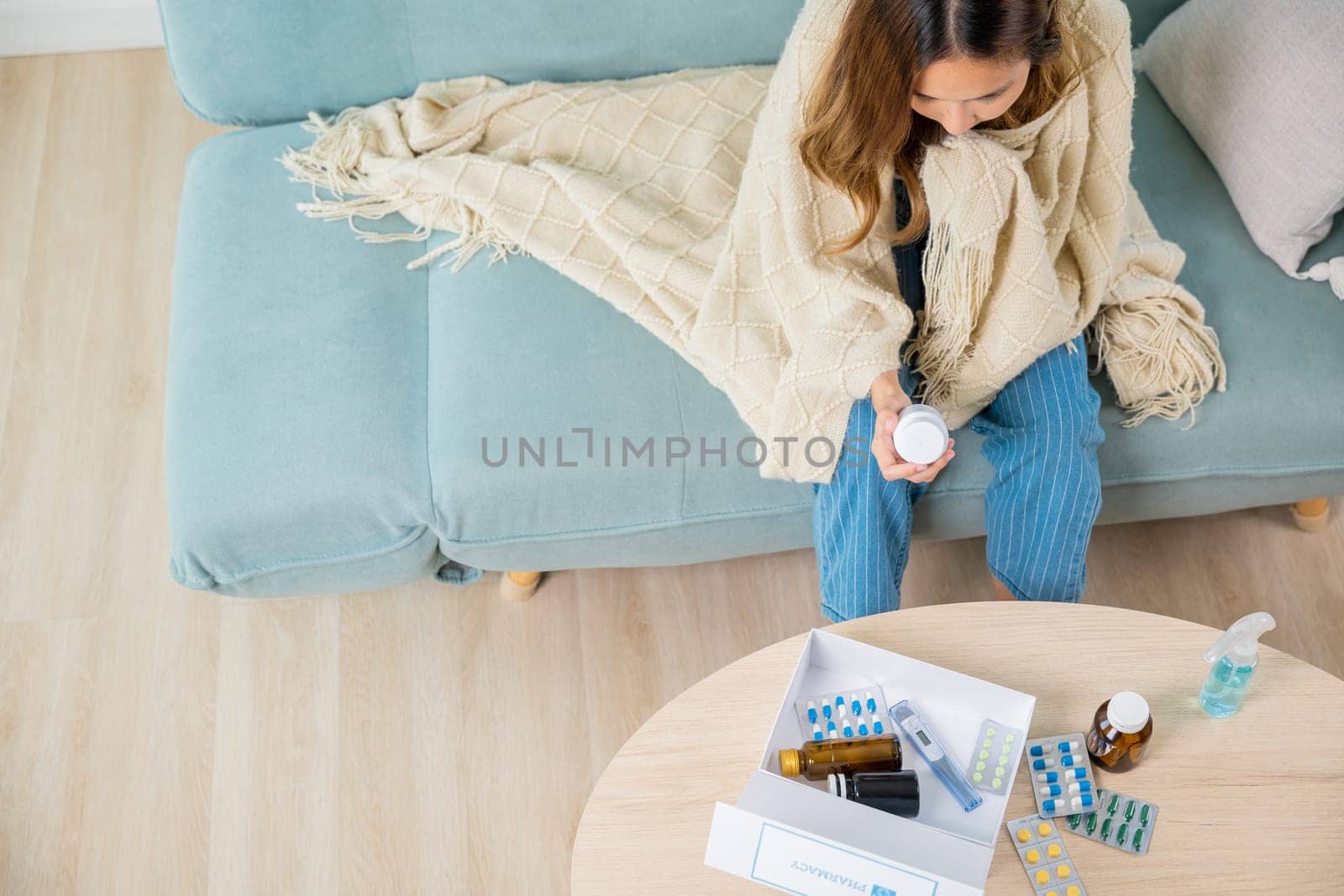 Asian young woman reading ingredient and hold bottle of drug on sofa at home, sick people reading information medicine label pills, female with flu virus, Health care and medicine concept