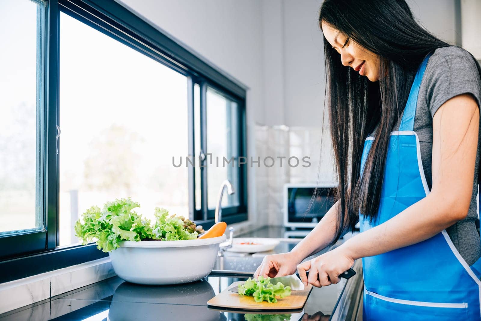 A smiling woman in an apron prepares a healthy dinner cutting vegetables for a delicious salad in her home kitchen. Close-up of a cheerful housewife making a nutritious meal.
