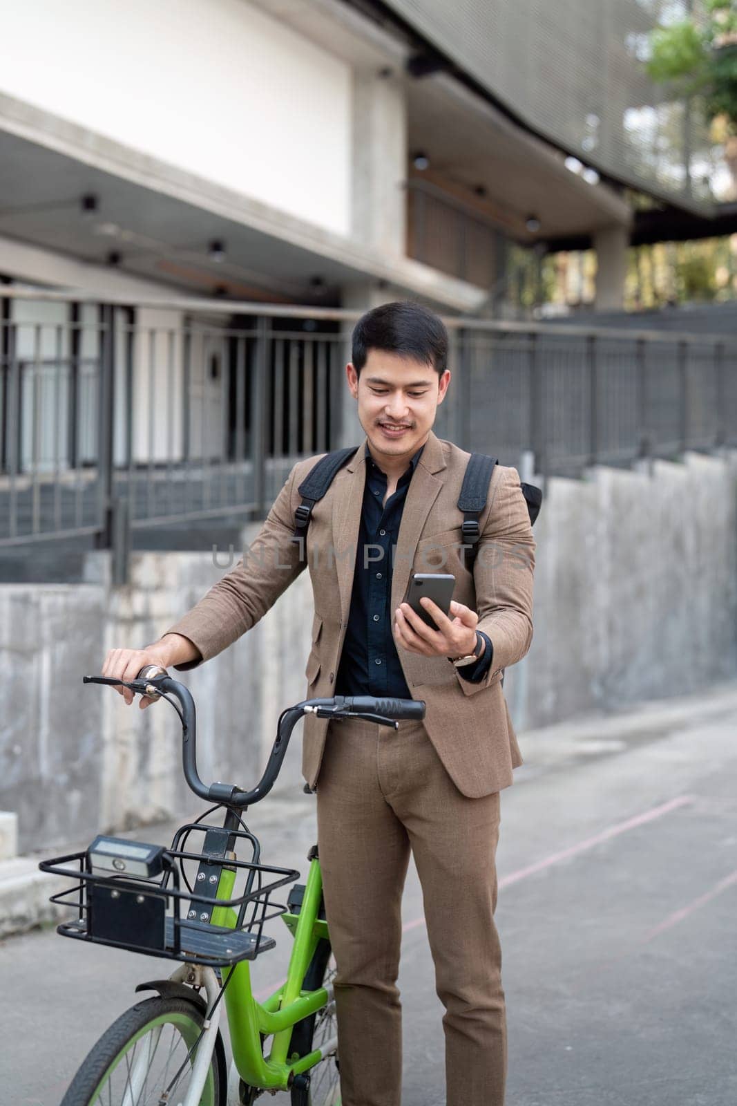 Asian businessman in a suit is riding a bicycle on the city streets for his morning commute to work. Eco transportation concept, sustainable lifestyle concept by nateemee