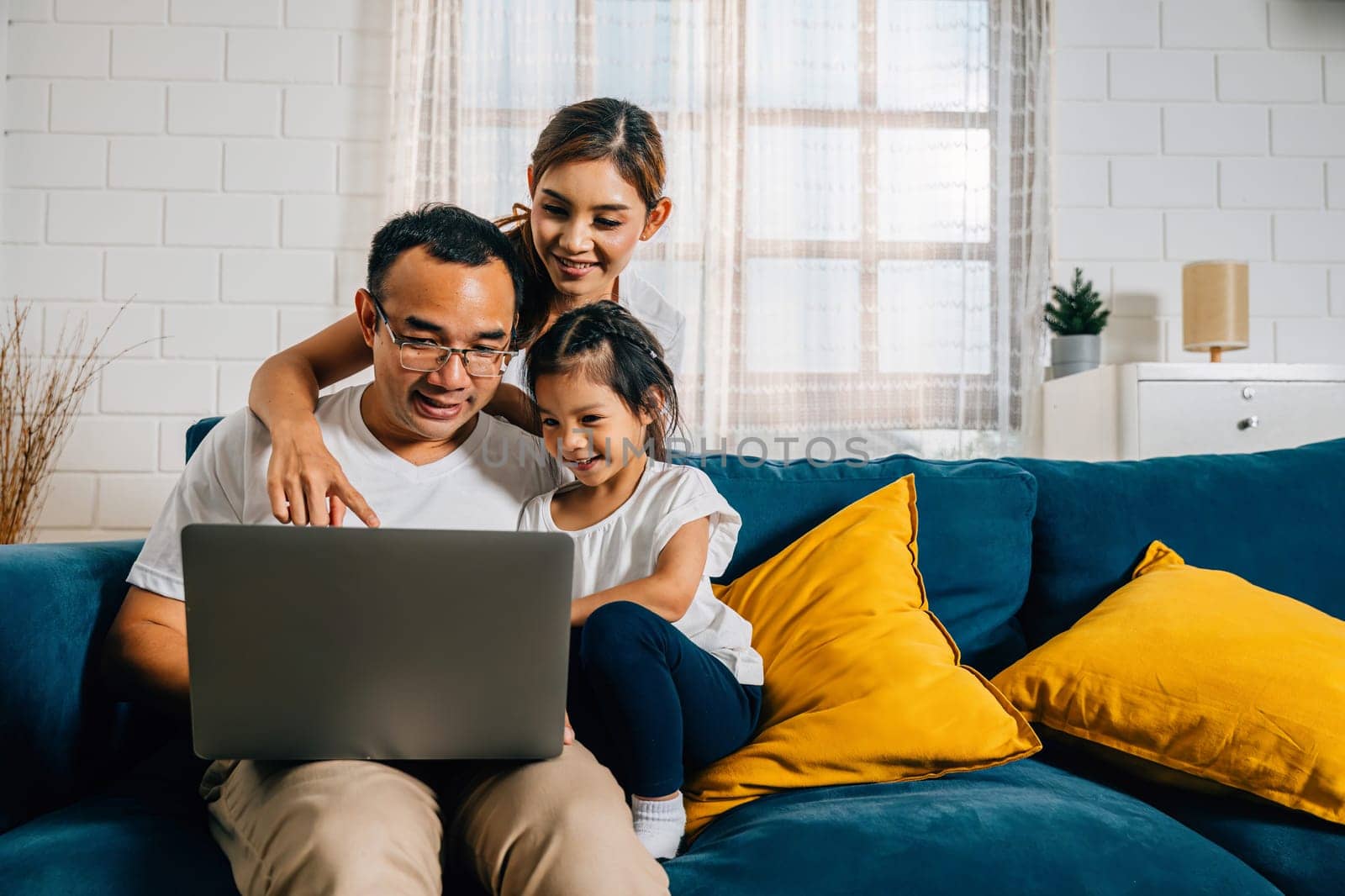 Family time on the couch as parents and kids engage with a laptop. A young man woman son and daughter search bond and smile in their modern home creating moments of happiness.