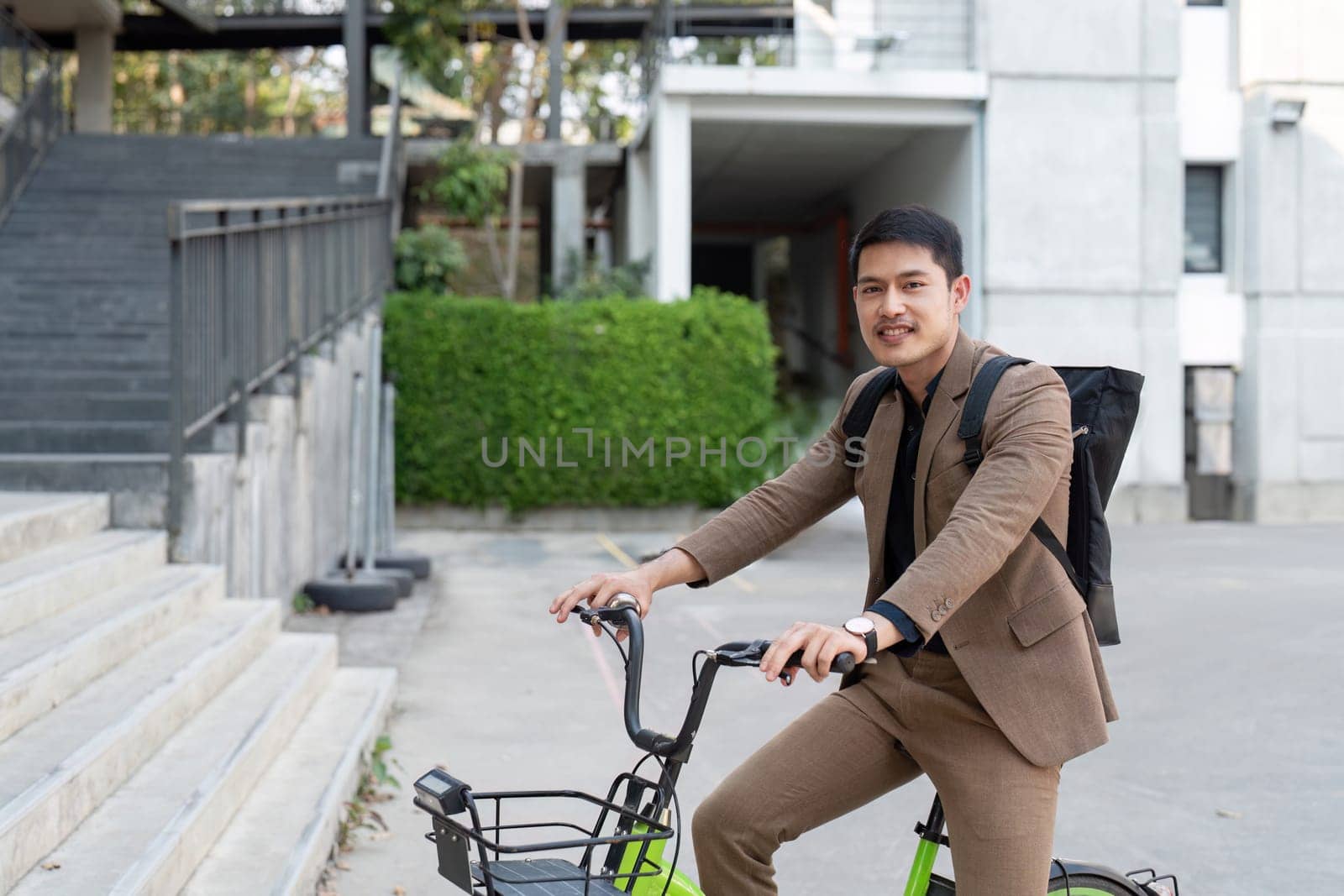 Asian businessman in a suit is riding a bicycle on the city streets for his morning commute to work. Eco transportation concept, sustainable lifestyle concept.