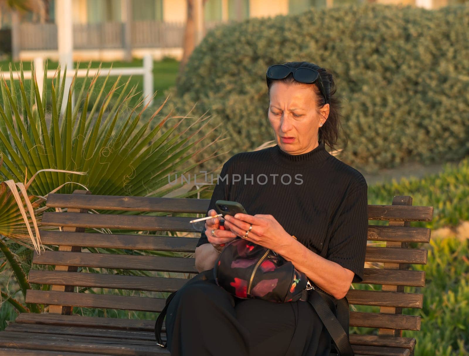 a woman with a cigarette and a phone sits on a bench near the Mediterranean Sea 2