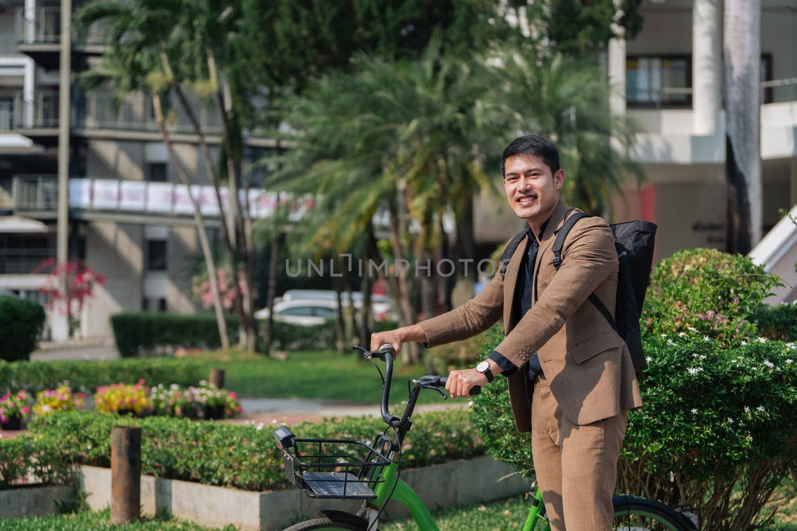 Young businessman in suit in city park bike to work eco friendly alternative vehicle green energy by itchaznong