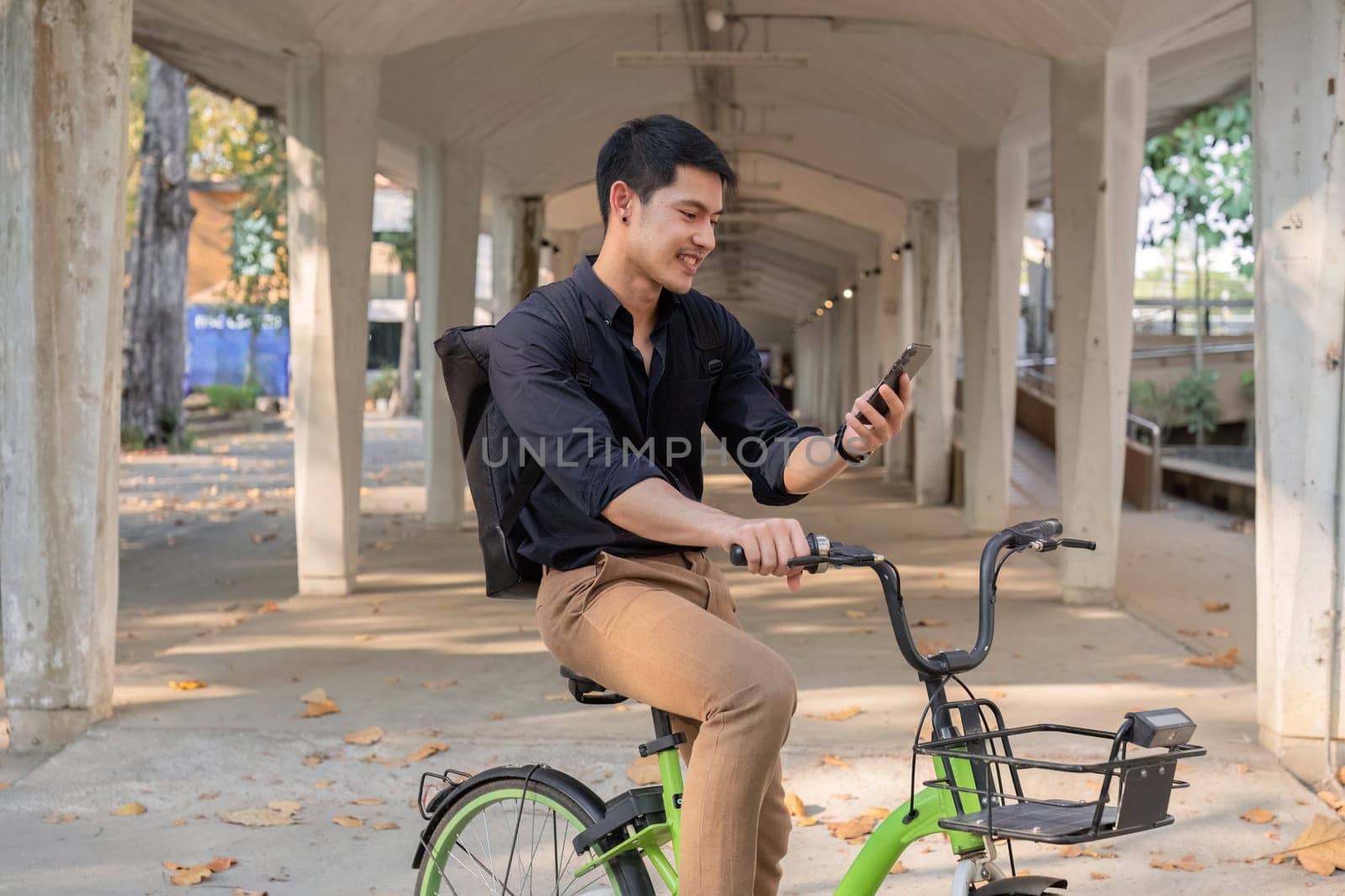 A young Asian businessman rides a bicycle to work. Standing outside the office talking on the phone and talking about business. Concept of reducing energy and reducing air pollution..