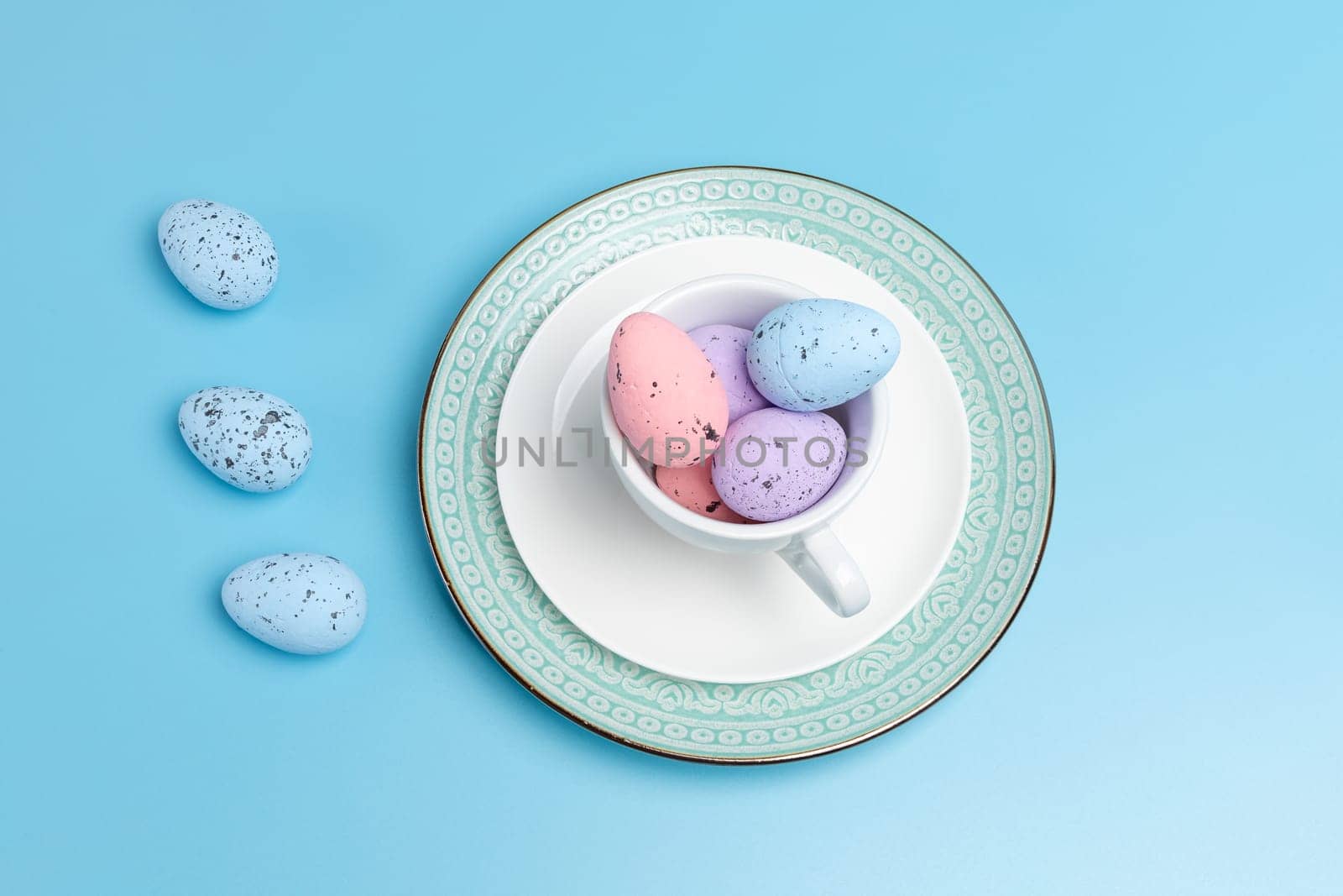 Porcelain cup with colored Easter eggs on a saucer and a dish with blue background. Top view.