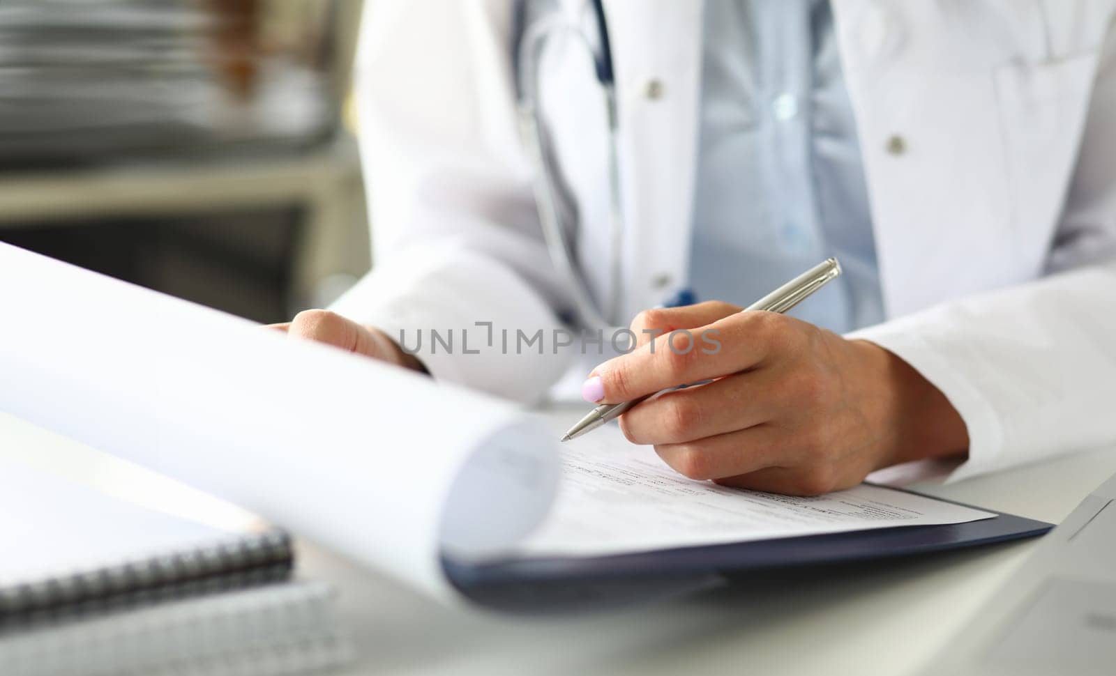 Hands of female GP making notes with silver pen while receiving visitor close-up