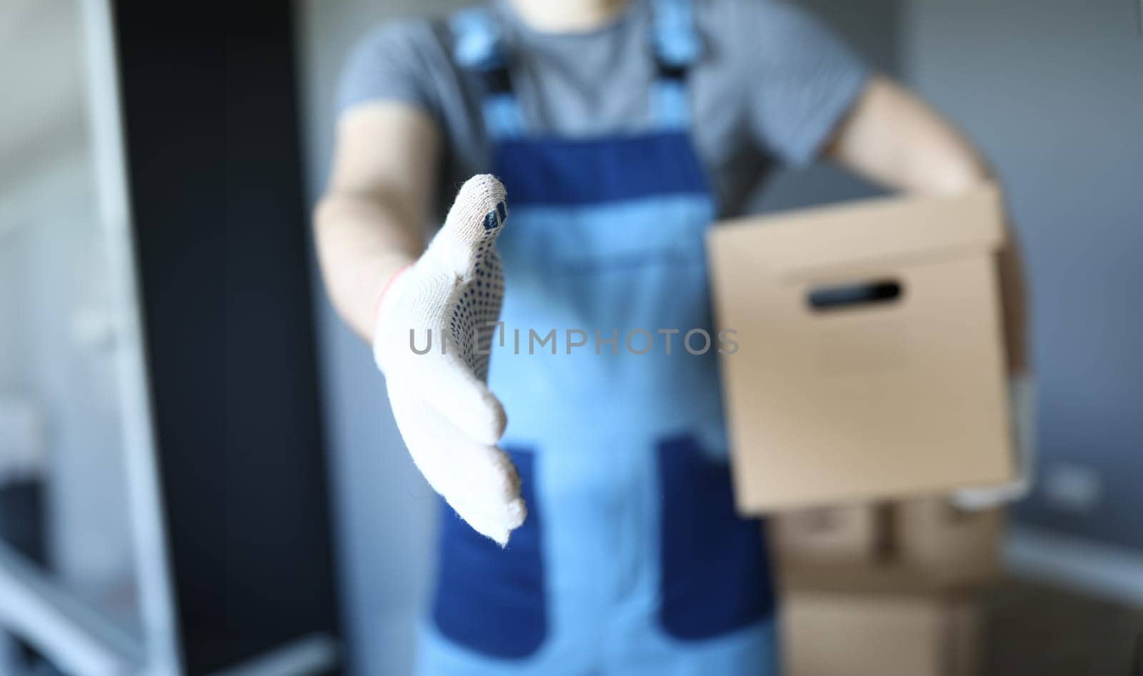 Close-up of male shake hand. Foreman holding cardboard box indoors. Delivery service. Interior design in new apartment. Purchased property. Renovation and handyman concept