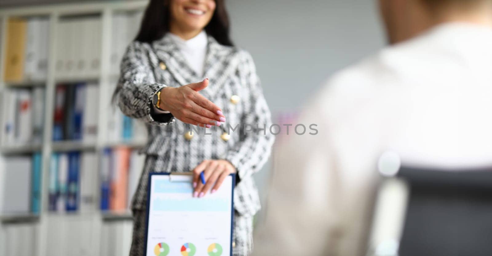 Close-up of cheerful employee extend hand for handshaking. Woman in luxury presentable suit. Clipboard with important diagram paper. Company and co-workers concept