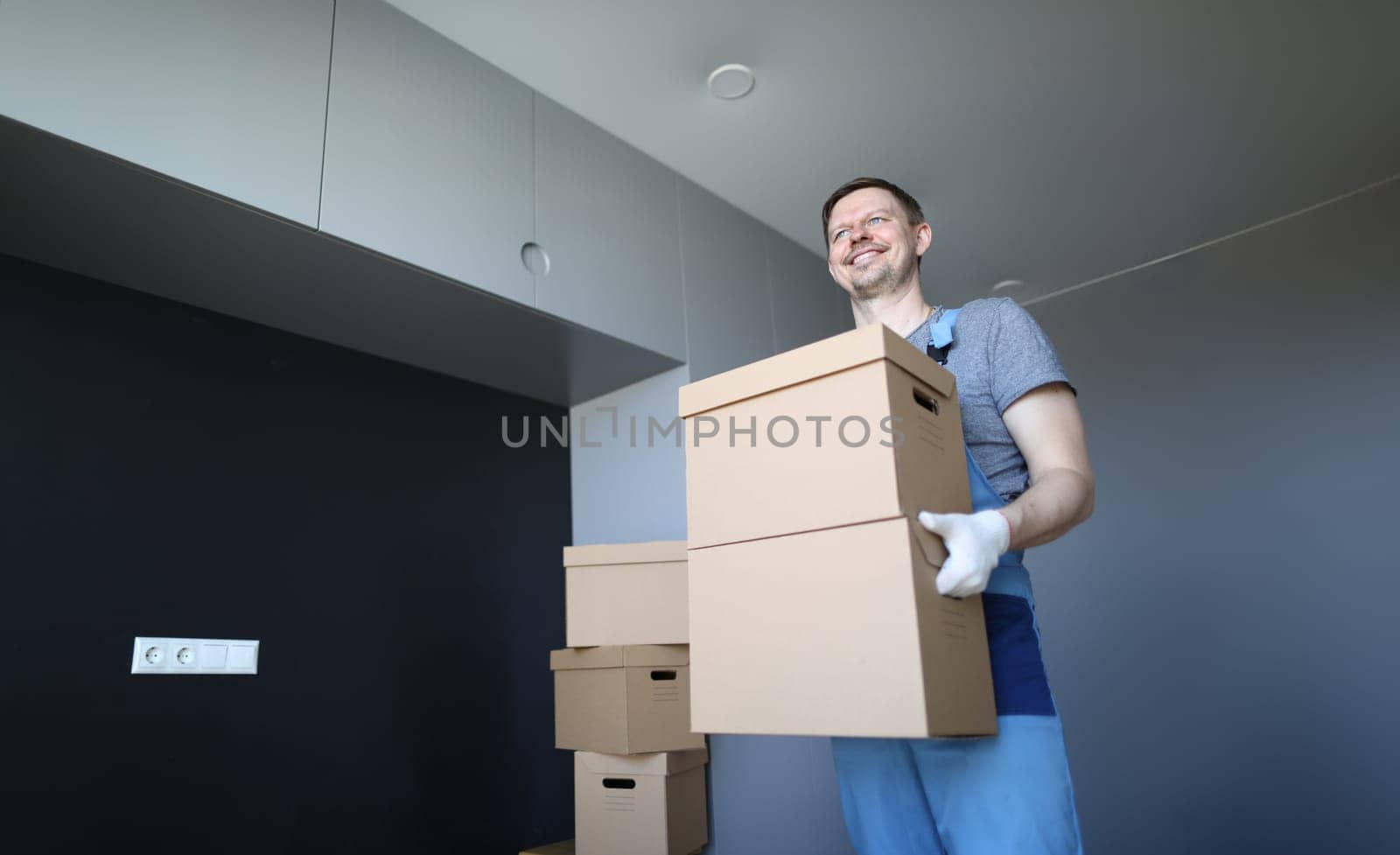 Portrait of smiling cheerful male carrying stack of boxes. Copy space in left side. Happy worker deliver cartons with personal stuff. Renovation and interior design concept