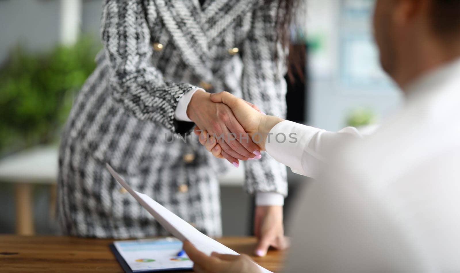 Close-up of business partners shaking hands. Young woman in presentable luxury suit holding document. Signing contract and make deal. Finance and economy concept