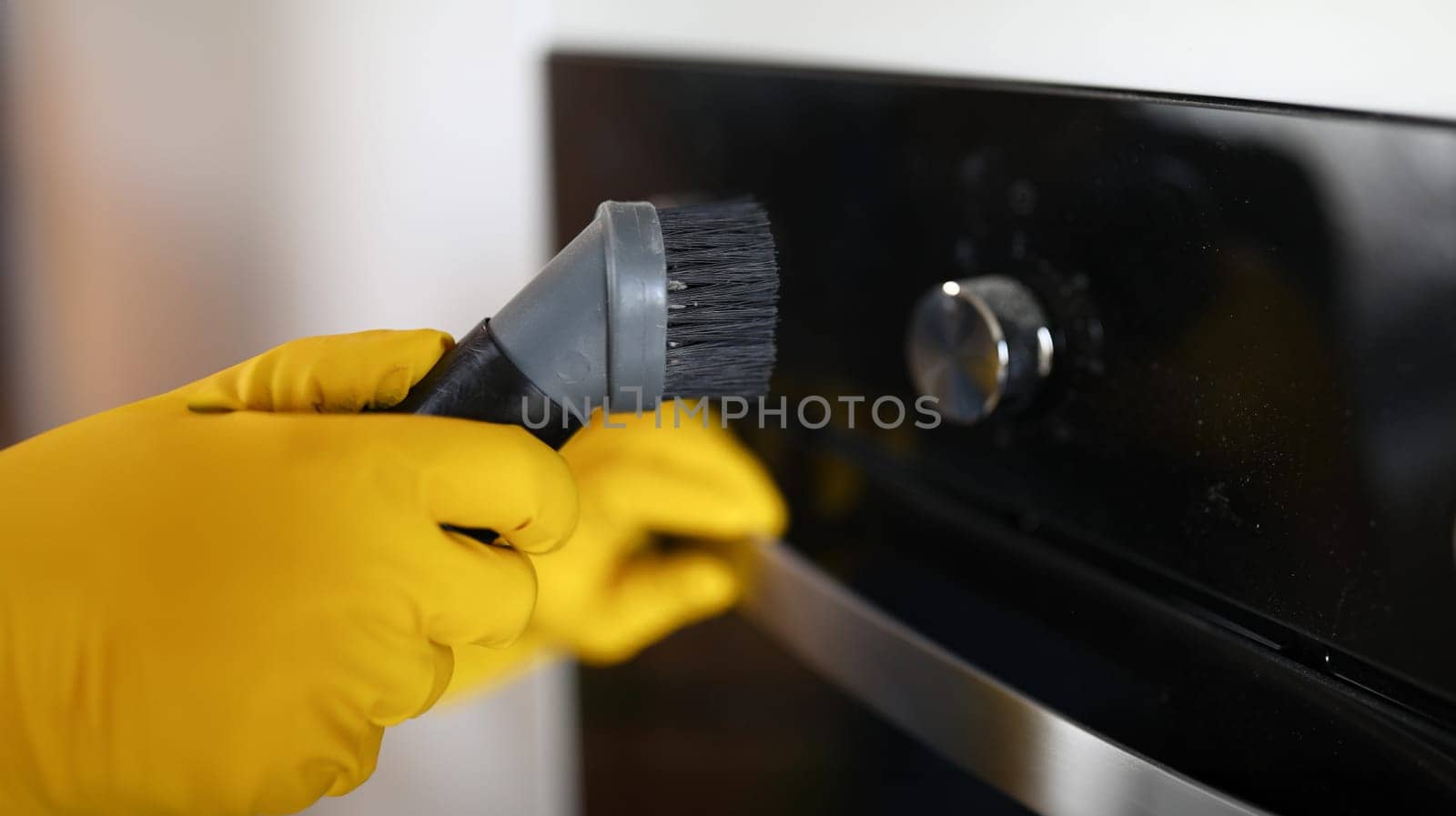 Close-up of persons hand cleaning cookstove display with nozzle of vacuum cleaner. Male in protective yellow gloves. Handyman and professional service concept