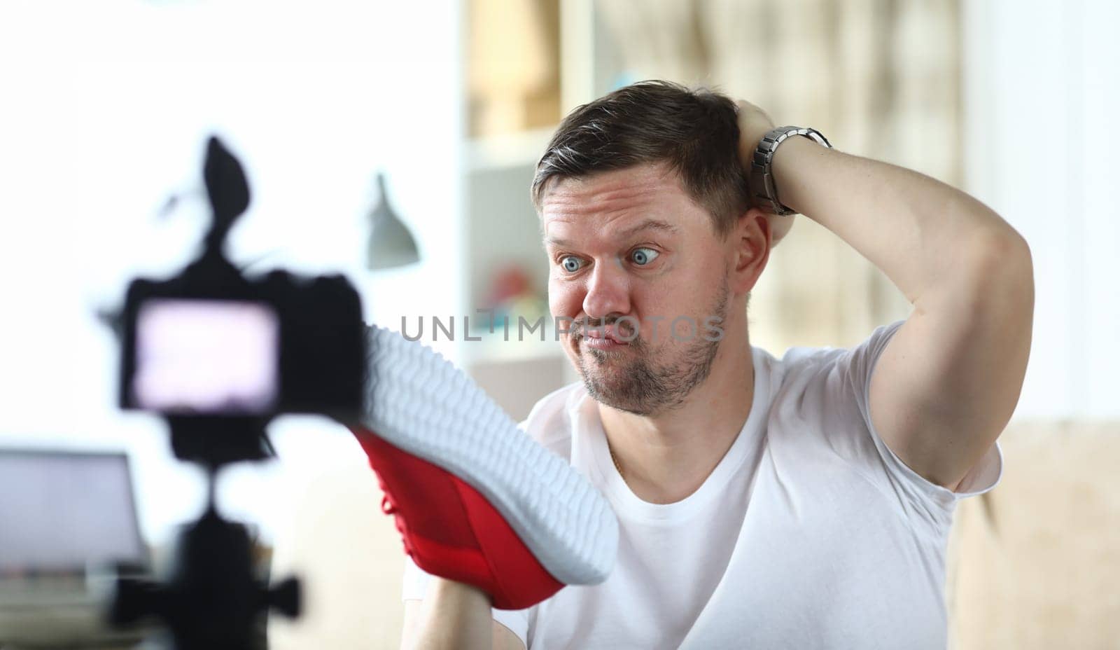 Close-up view of man scratching back of head and thinking followers reviews about new red sneakers. Male with good mimic. Beginner vlogger and technology concept
