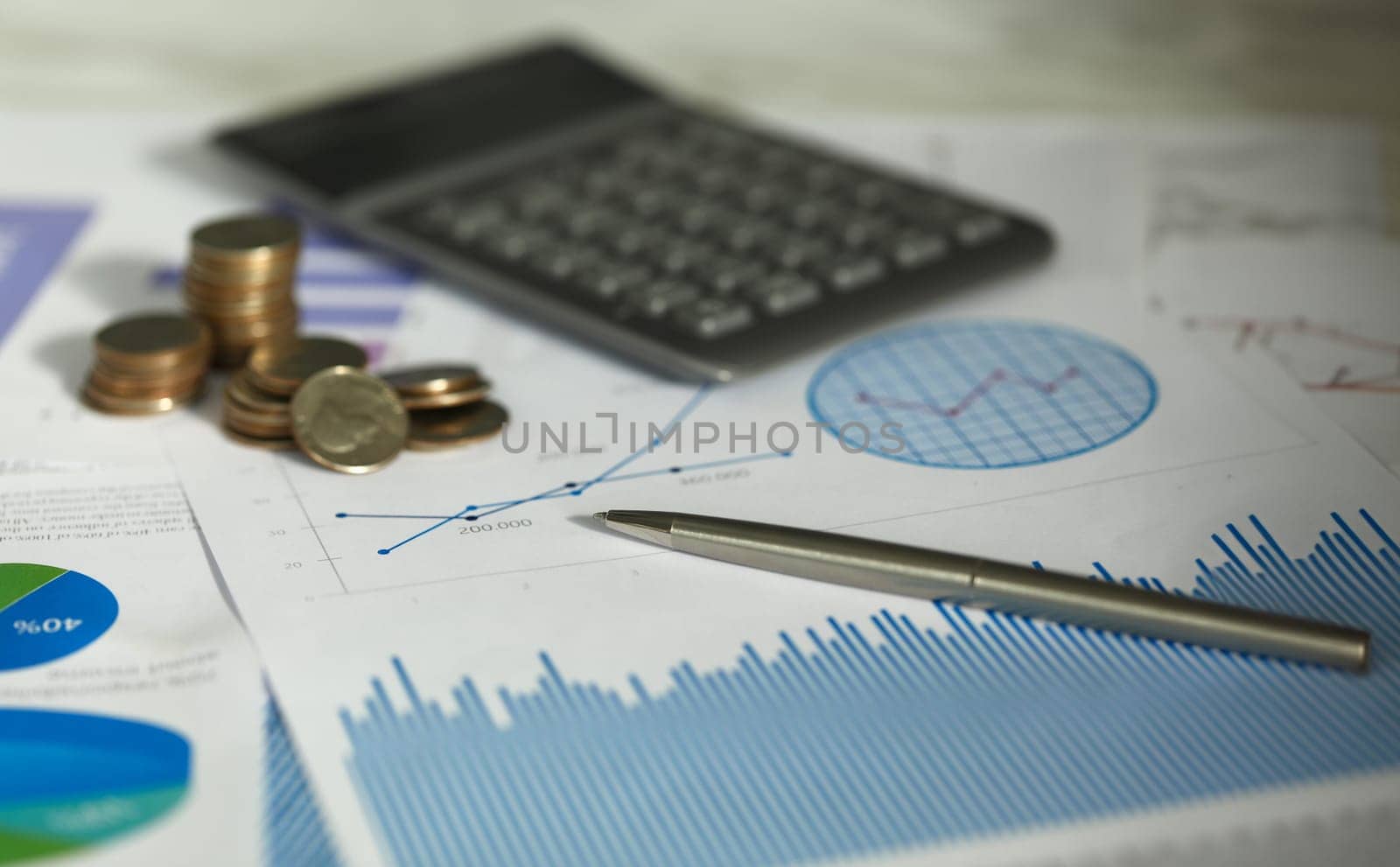 Close-up view of paper with business graphs and diagrams. Calculator and stack of coins on document. Statistics and accounting. Finance and economy growth concept