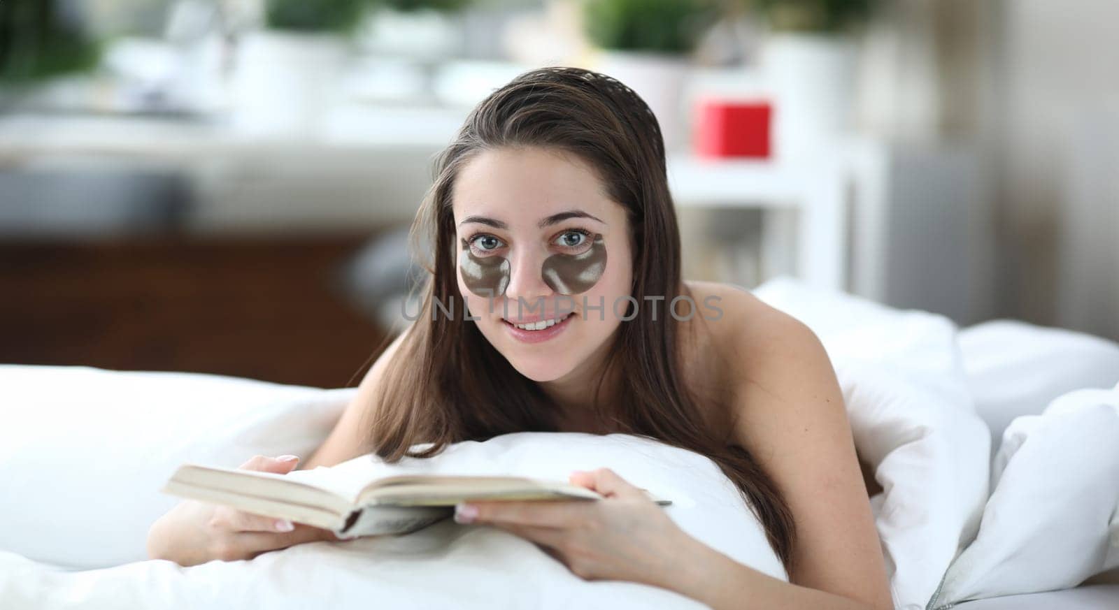 Portrait of beautiful female person reading during spa treatments. Wonderful woman relaxing from moisturizing skin under eyes. Beauty and cosmetics concept