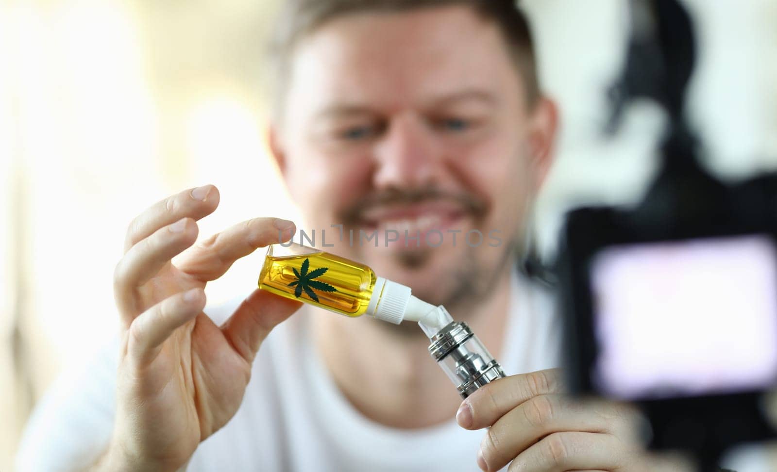 Close-up view of smiling middle-aged man dropping cannabinoid oil into special container. Happy male filming process on video camera. Beginner blogger making experiment